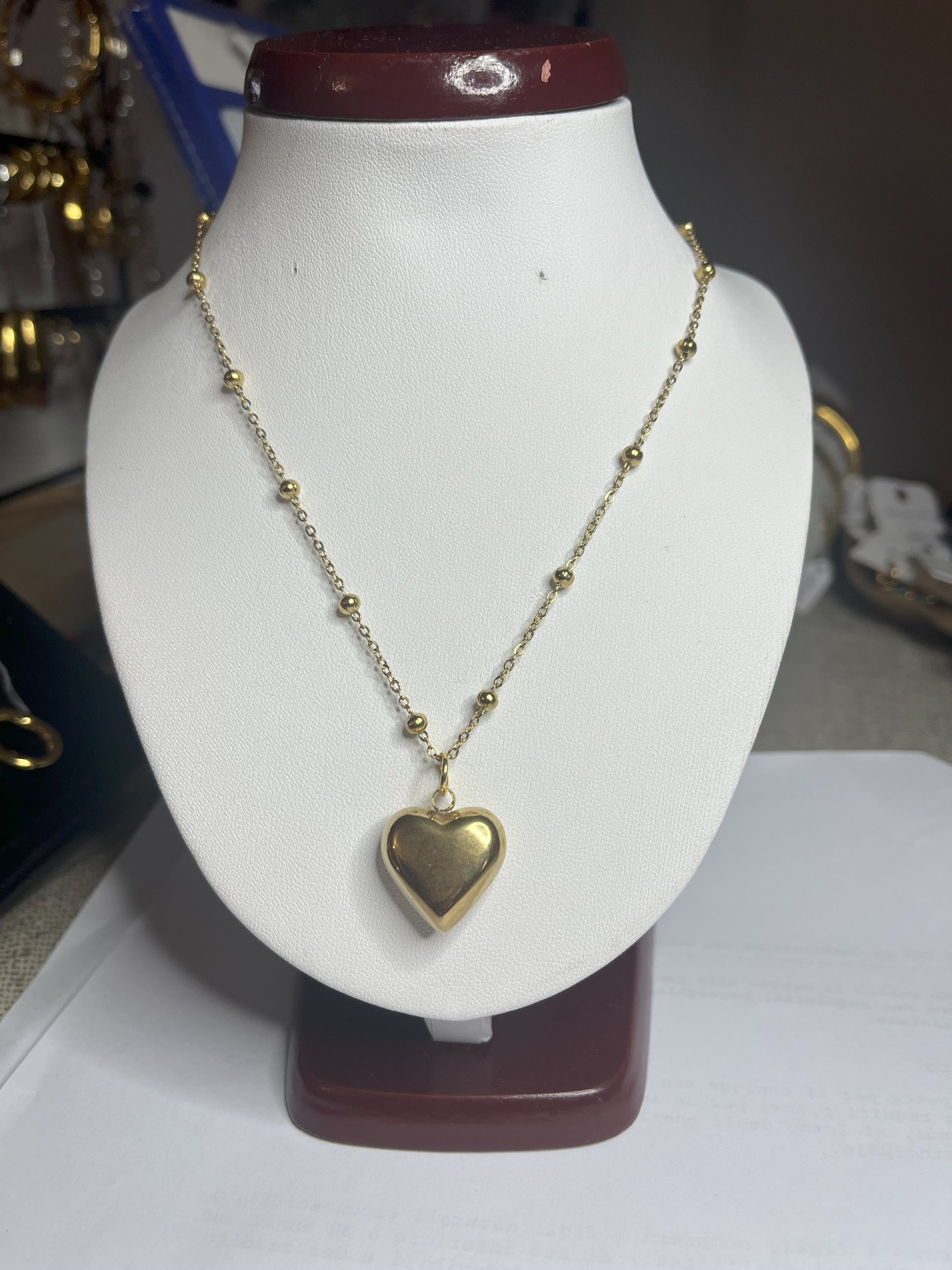 Collana Allegra in acciaio premium con catena decorata da sfere e ciondolo cuore, variante placcato oro, esposta su busto espositore bianco
