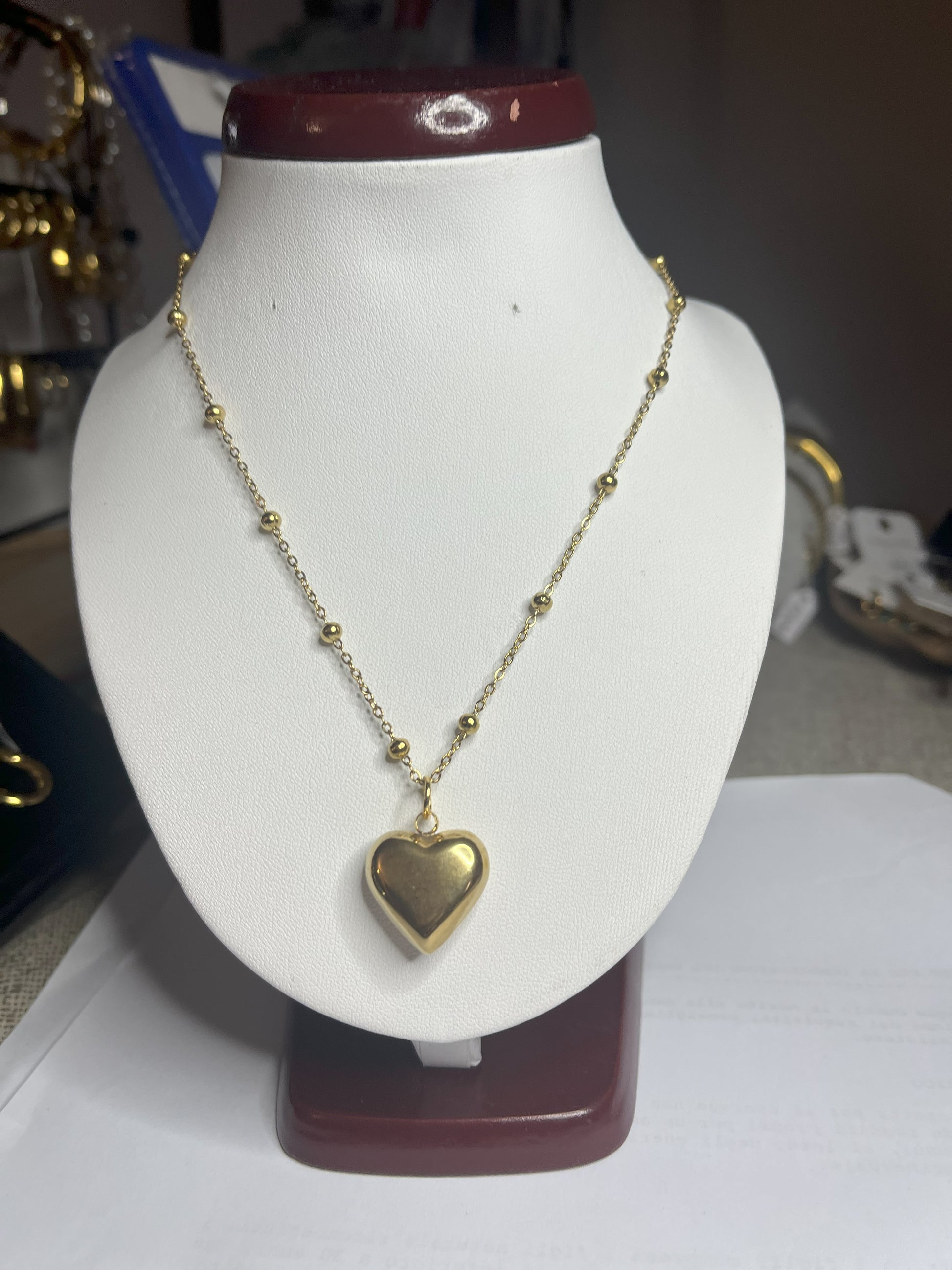 Collana Allegra in acciaio premium con catena decorata da sfere e ciondolo cuore, variante placcato oro, esposta su busto espositore bianco