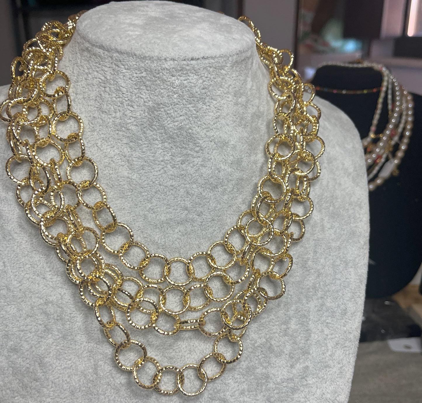 Collana elegante in alluminio placcato oro con quadrupla catena e cerchi intrecciati, esposta su busto bianco