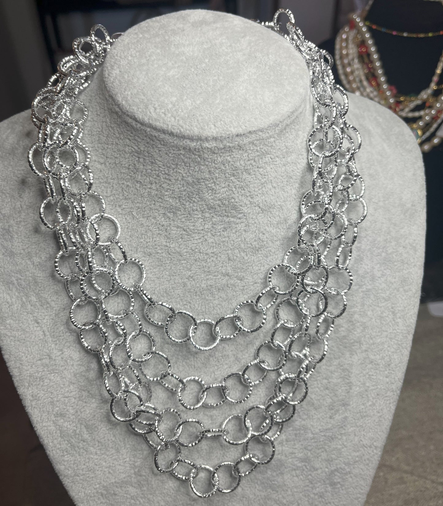 Collana elegante in alluminio placcato argento con quadrupla catena e cerchi intrecciati, esposta su busto bianco
