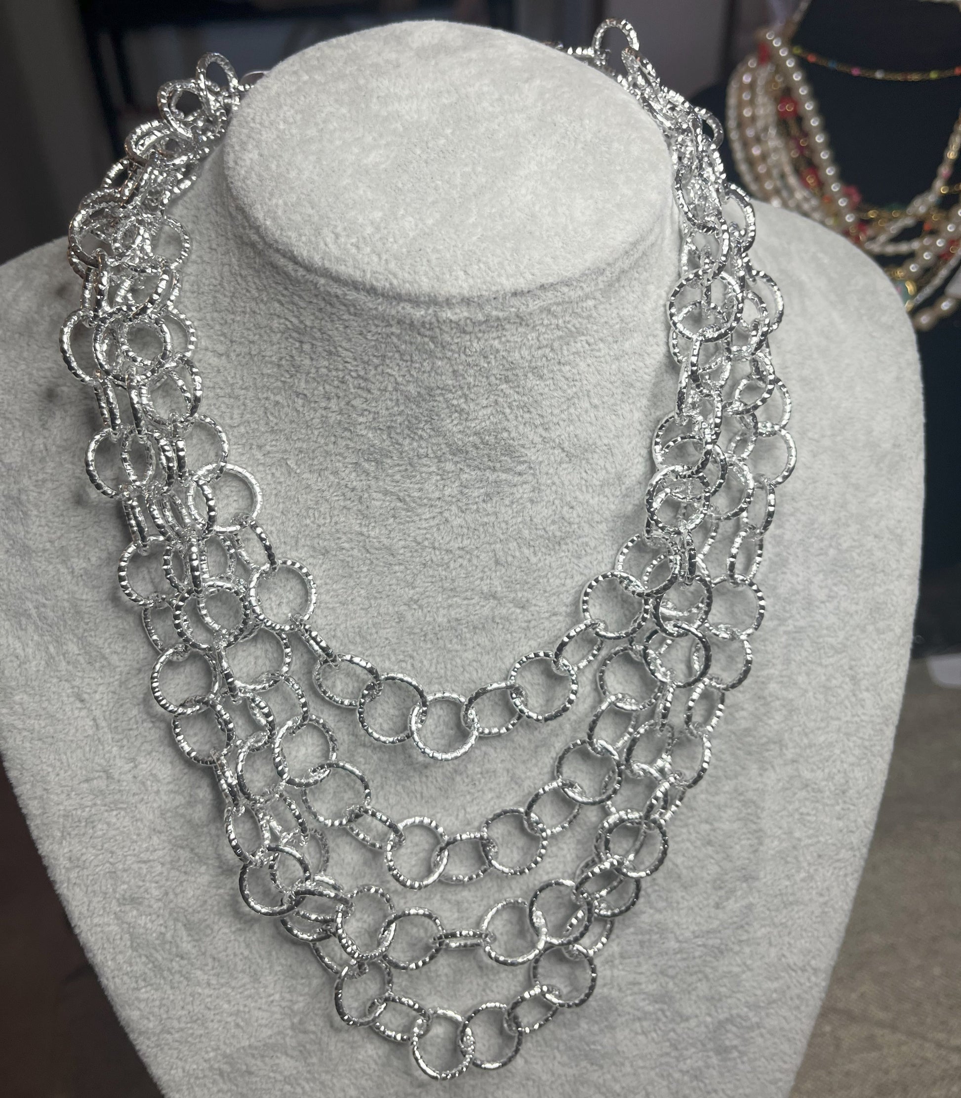 Collana elegante in alluminio placcato argento con quadrupla catena e cerchi intrecciati, esposta su busto bianco