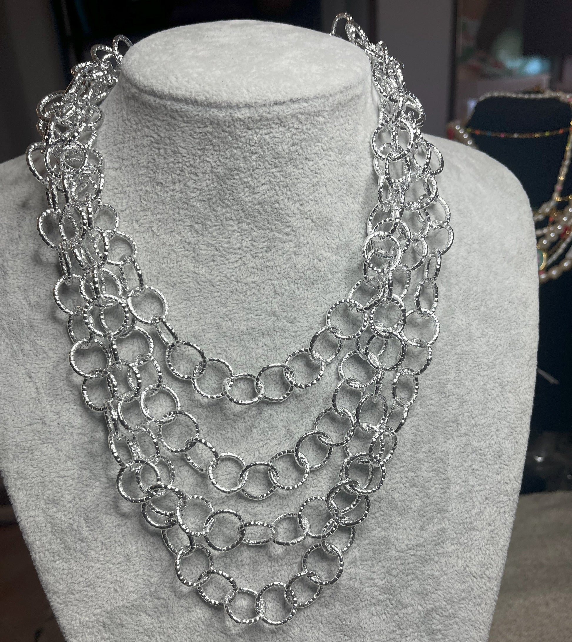 Collana elegante in alluminio placcato argento con quadrupla catena e cerchi intrecciati, esposta su busto bianco