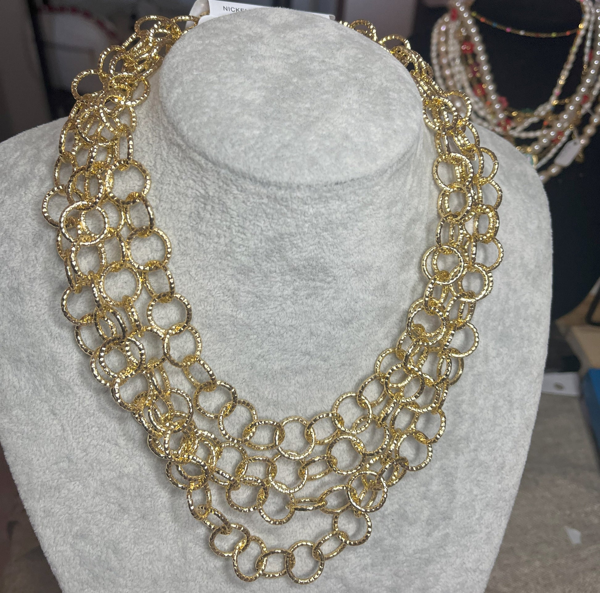 Collana elegante in alluminio placcato oro con quadrupla catena e cerchi intrecciati, esposta su busto bianco