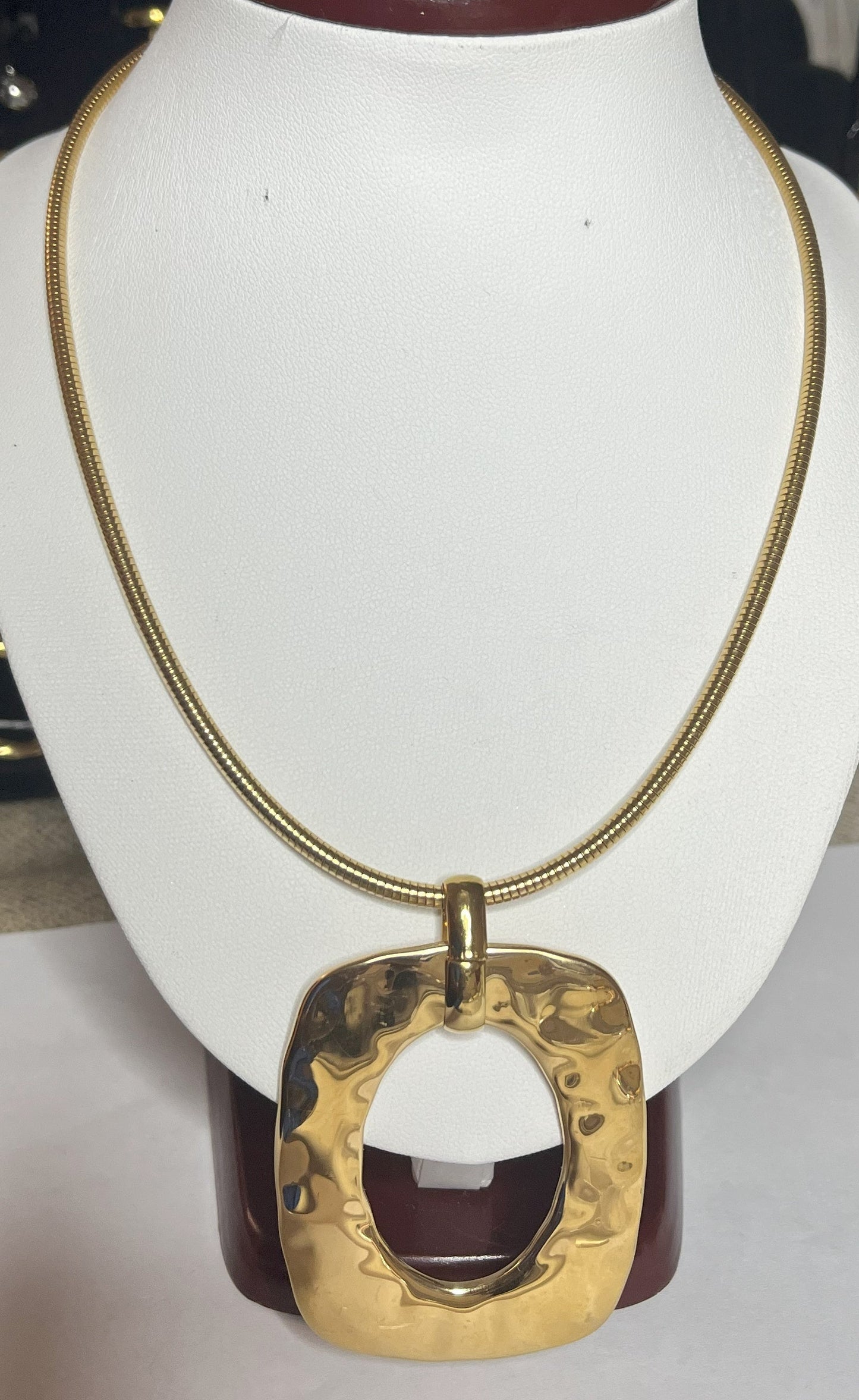 Collana Charlize in acciaio inossidabile placcato oro con catena a maglia serpente e pendente geometrico quadrato, esposta su busto bianco