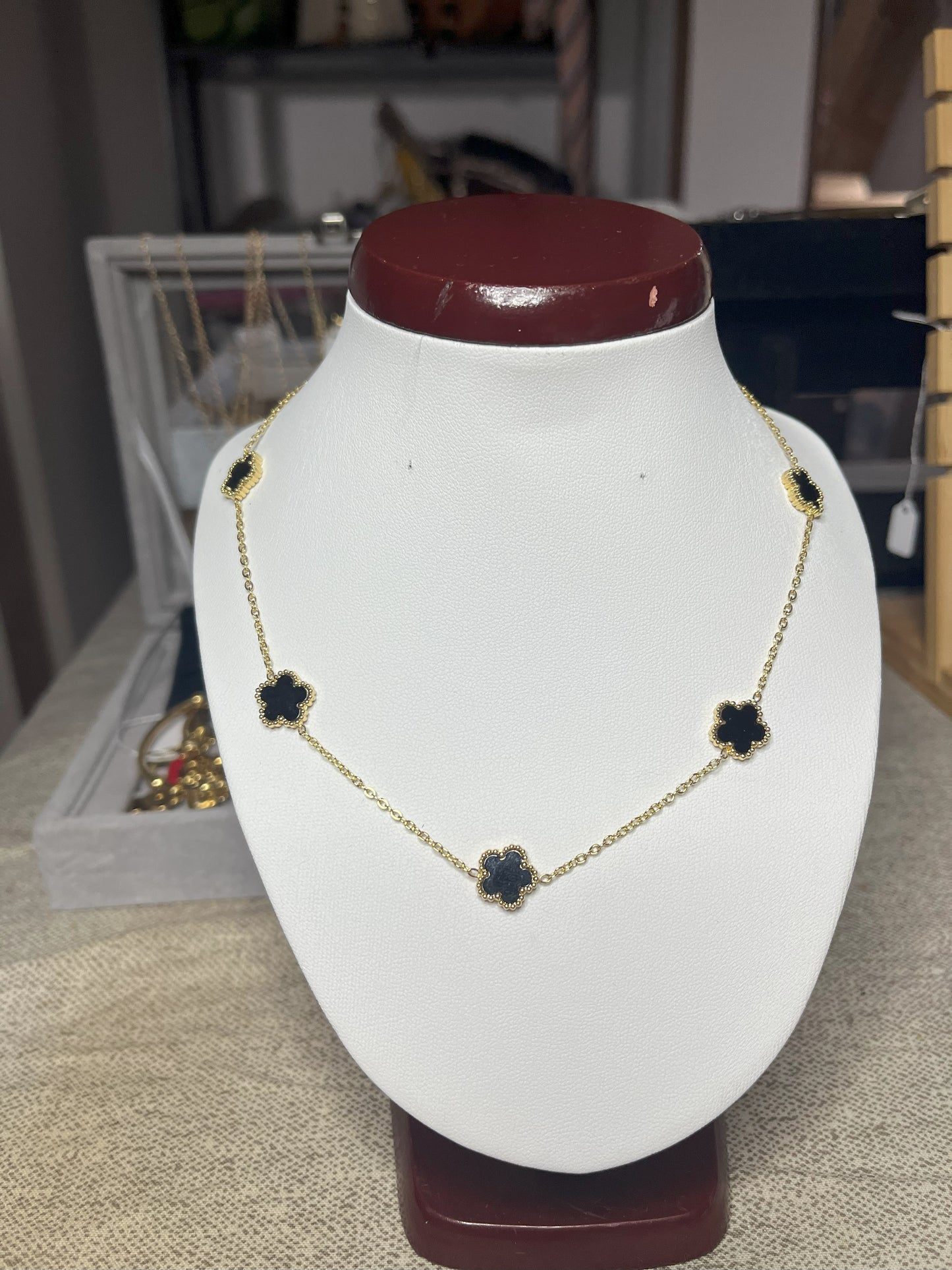 Collana Élégance Suprême in ottone dorato con cinque elementi floreali neri disposti simmetricamente, esposta su busto bianco, design elegante e raffinato stile italiano