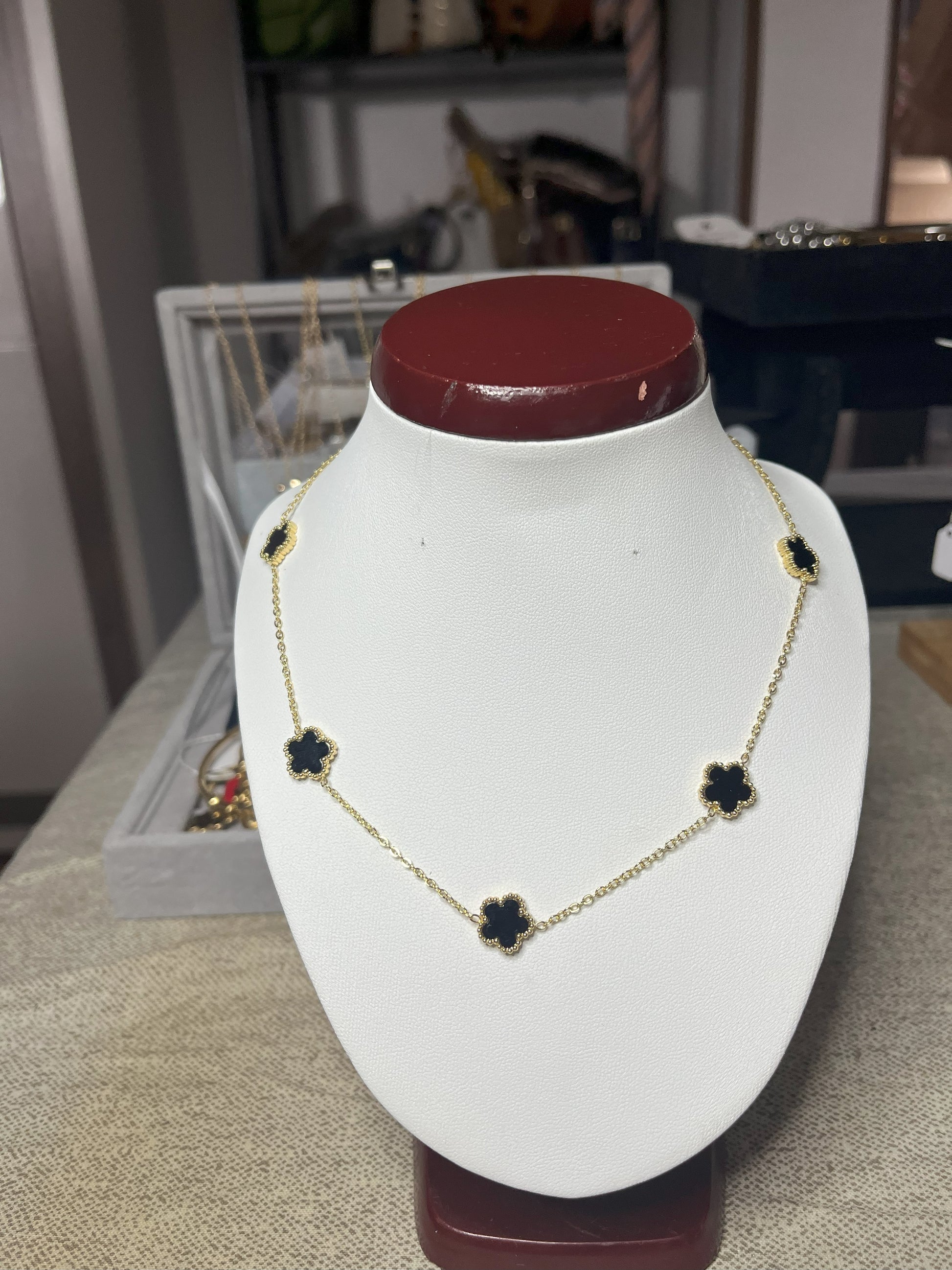 Collana Élégance Suprême in ottone dorato con cinque elementi floreali neri disposti simmetricamente, esposta su busto bianco, design elegante e raffinato stile italiano