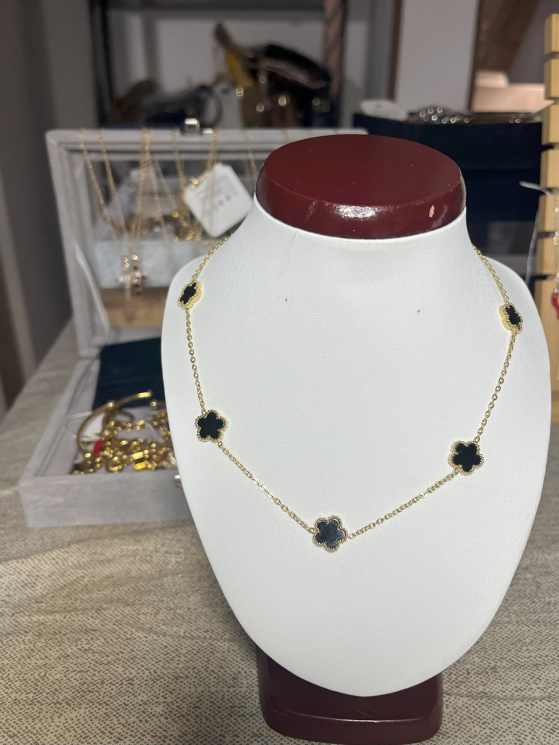 Collana Élégance Suprême in ottone dorato con cinque elementi floreali neri disposti simmetricamente, esposta su busto bianco, design elegante e raffinato stile italiano