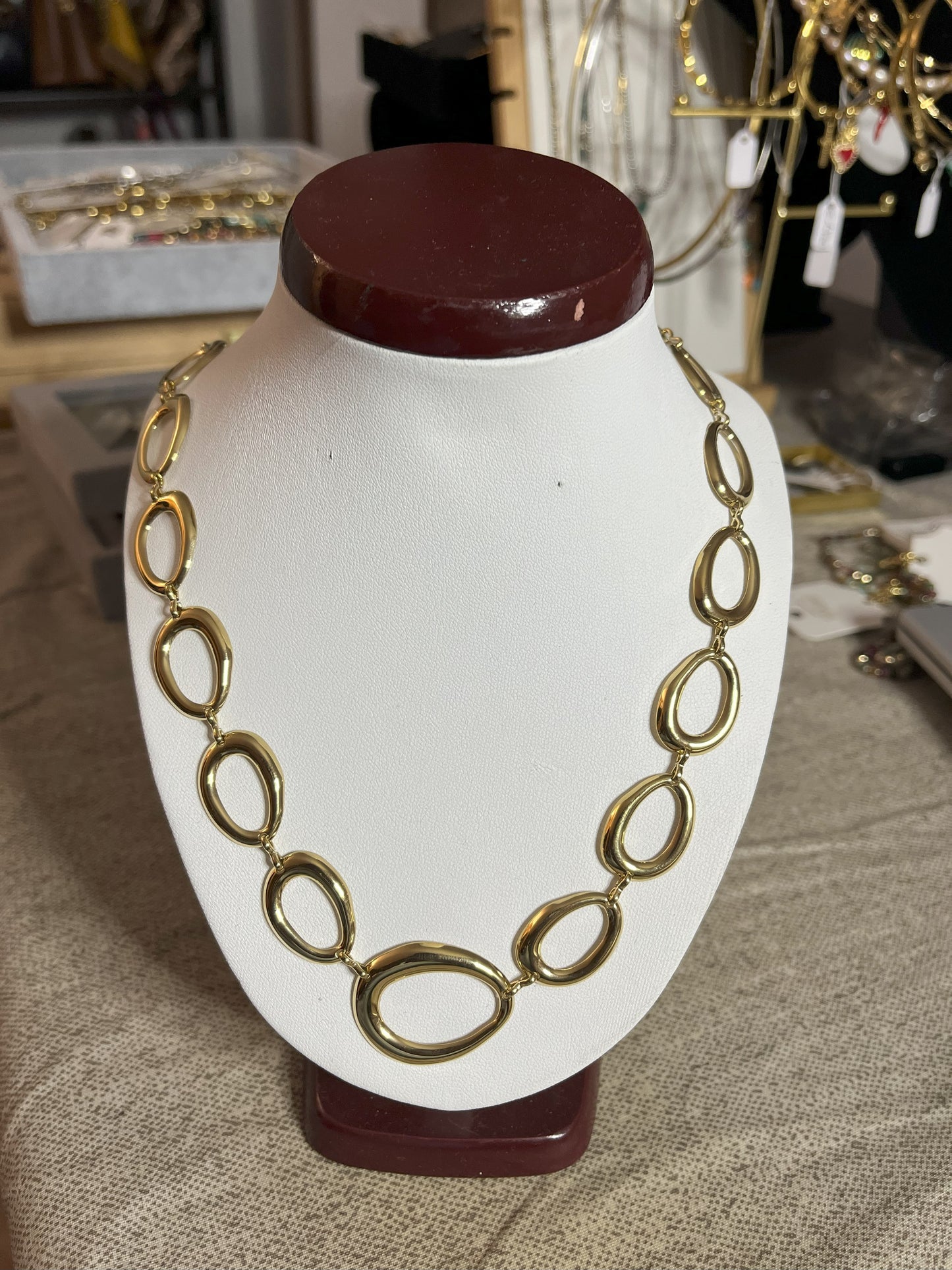 Collana Golden Embrace con anelli ovali dorati concatenati placcati oro su espositore bianco, design elegante statement per donna