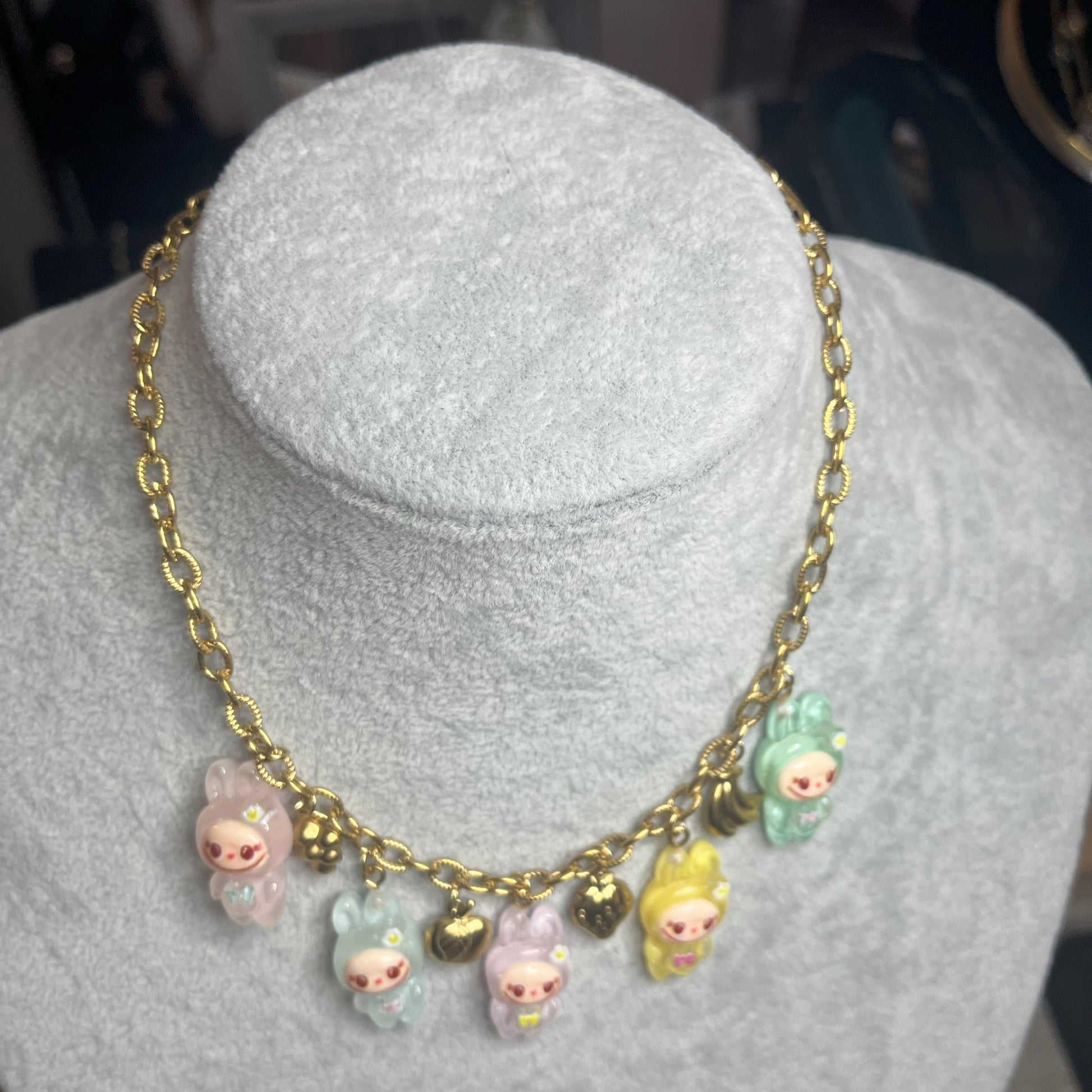 Collana con catena dorata e charms kawaii colorati a forma di personaggi cute, esposta su busto bianco