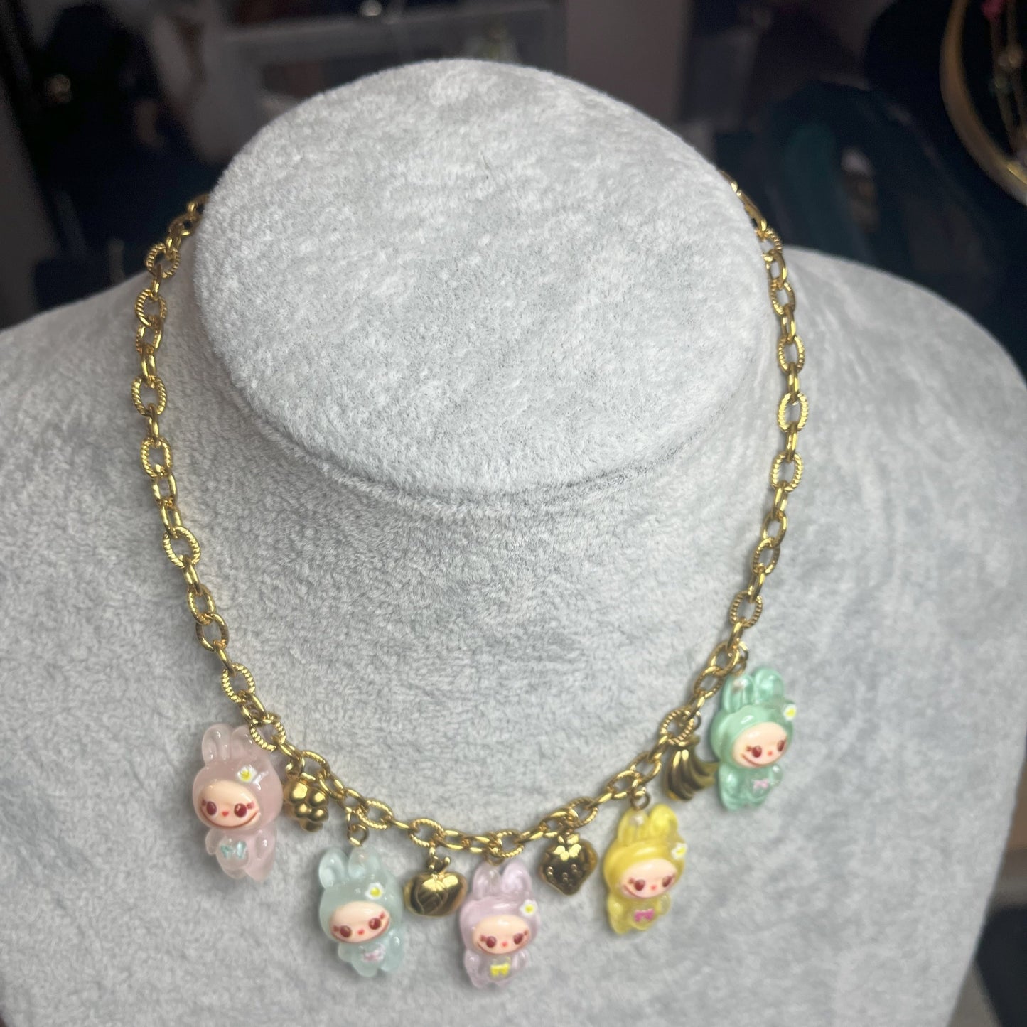 Collana con catena dorata e charms kawaii colorati a forma di personaggi cute, esposta su busto bianco
