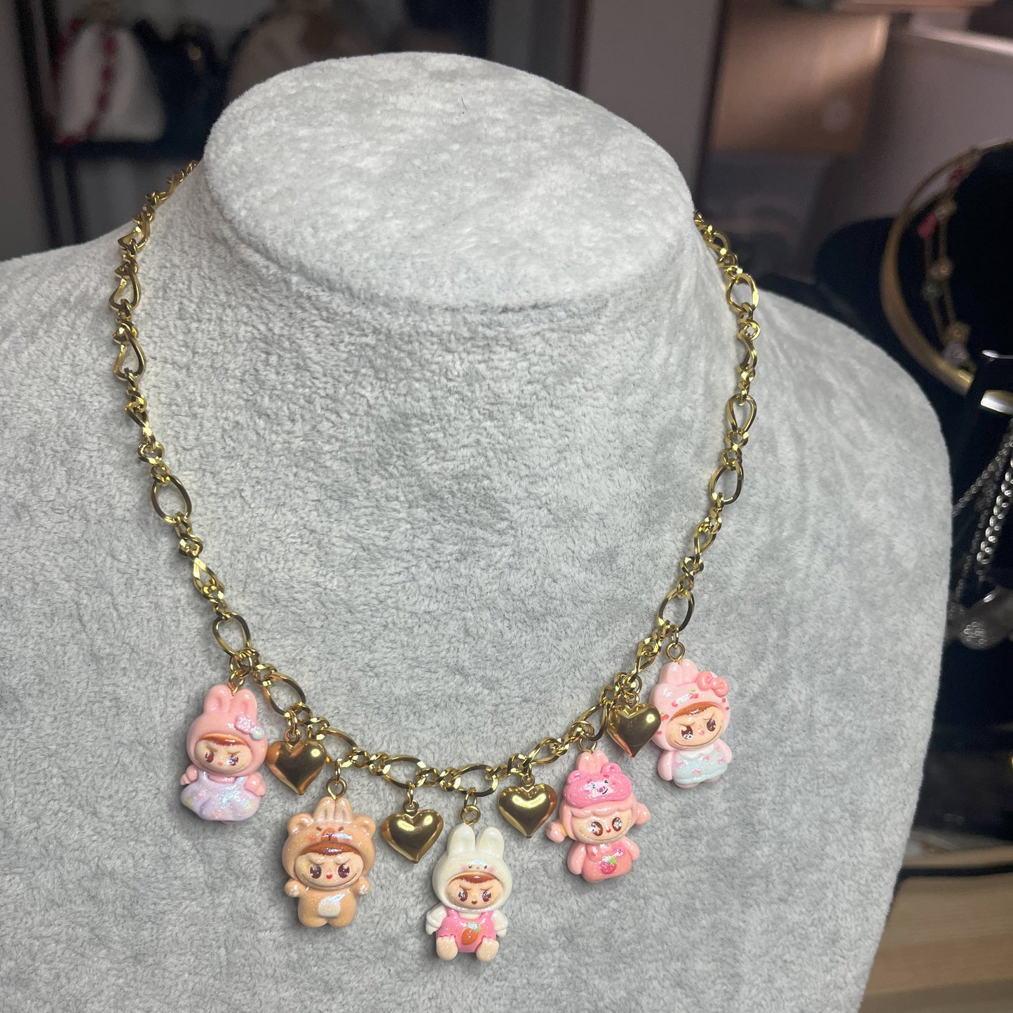 Collana con catena dorata e charms kawaii colorati a forma di personaggi cute, esposta su busto bianco