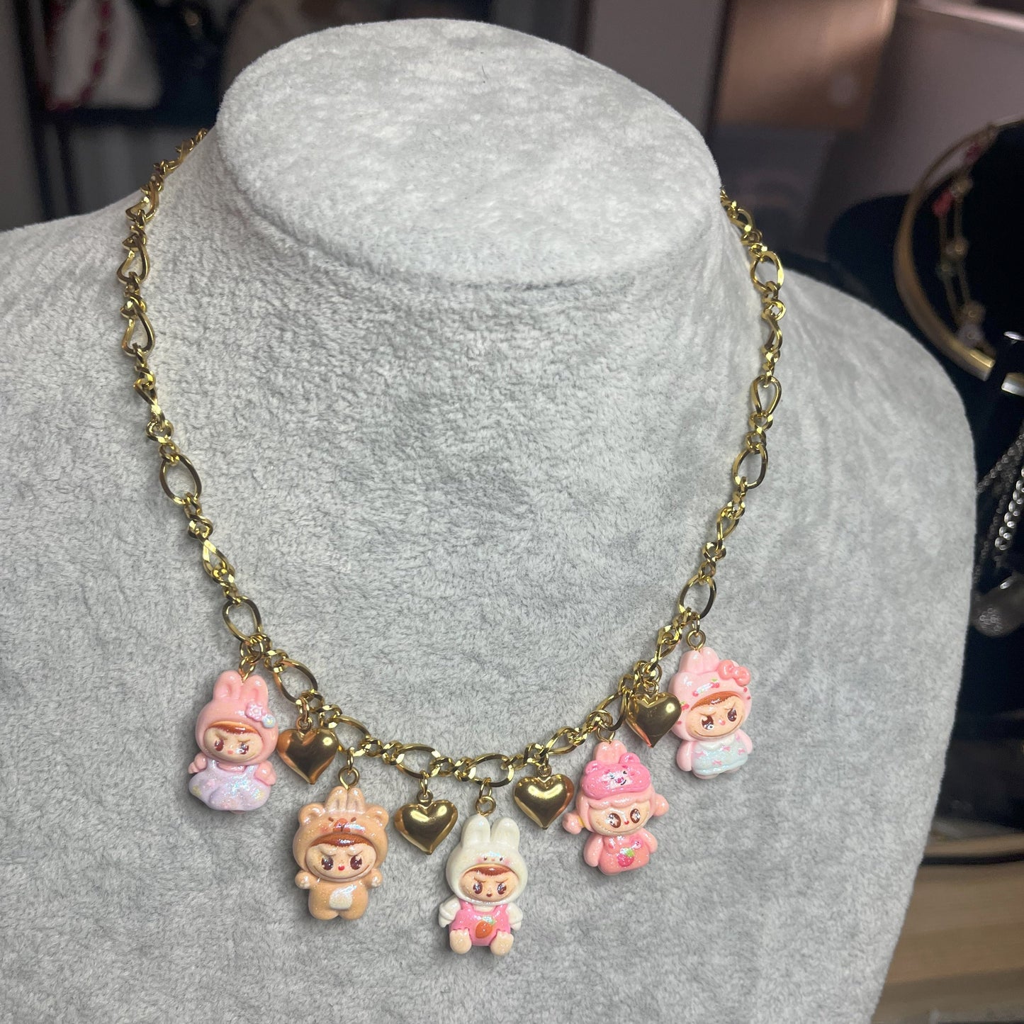 Collana con catena dorata e charms kawaii colorati a forma di personaggi cute, esposta su busto bianco