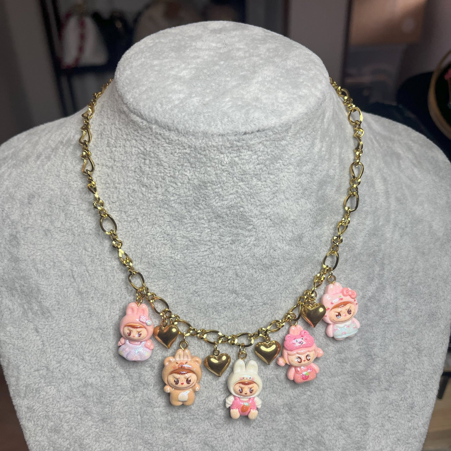Collana con catena dorata e charms kawaii colorati a forma di personaggi cute, esposta su busto bianco