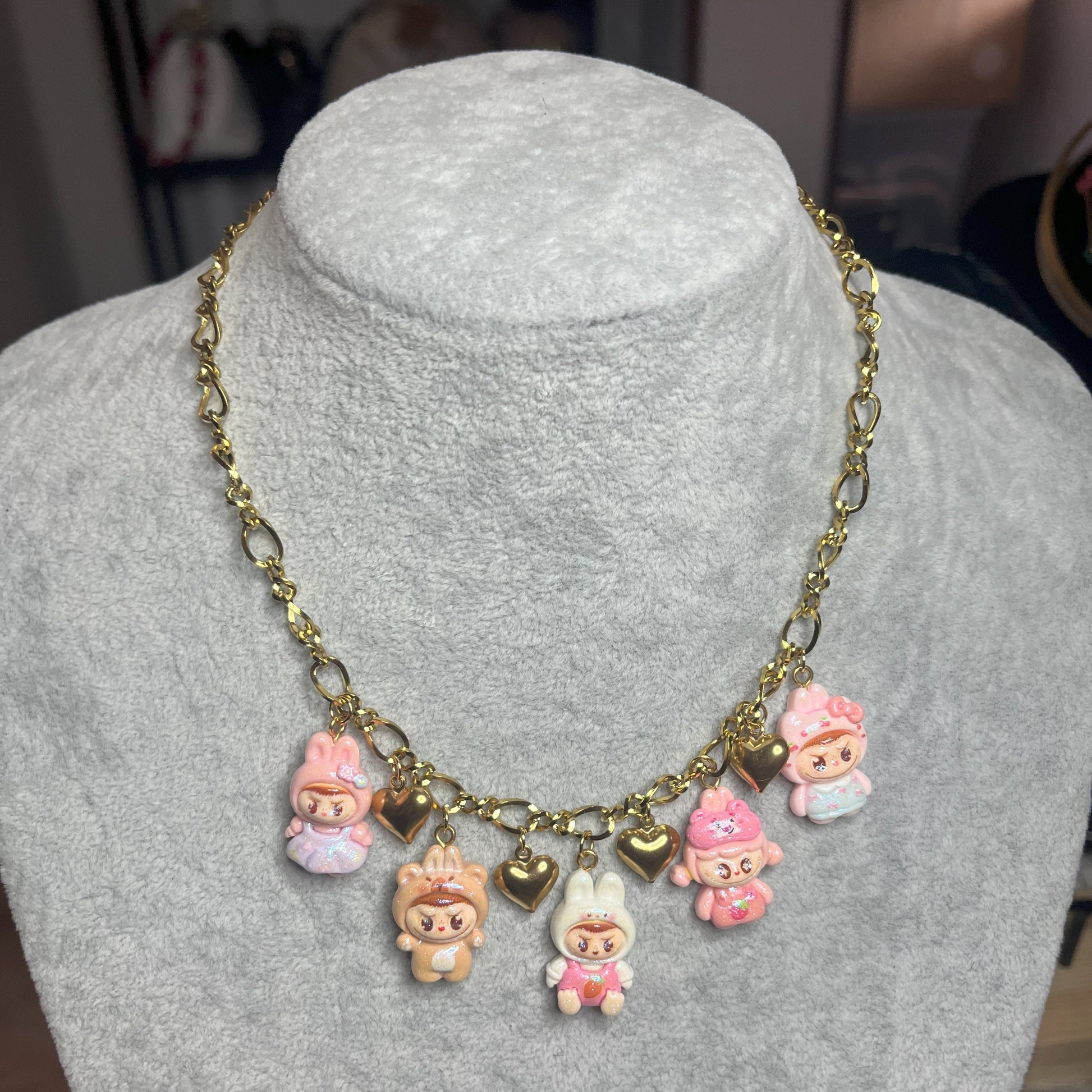 Collana con catena dorata e charms kawaii colorati a forma di personaggi cute, esposta su busto bianco