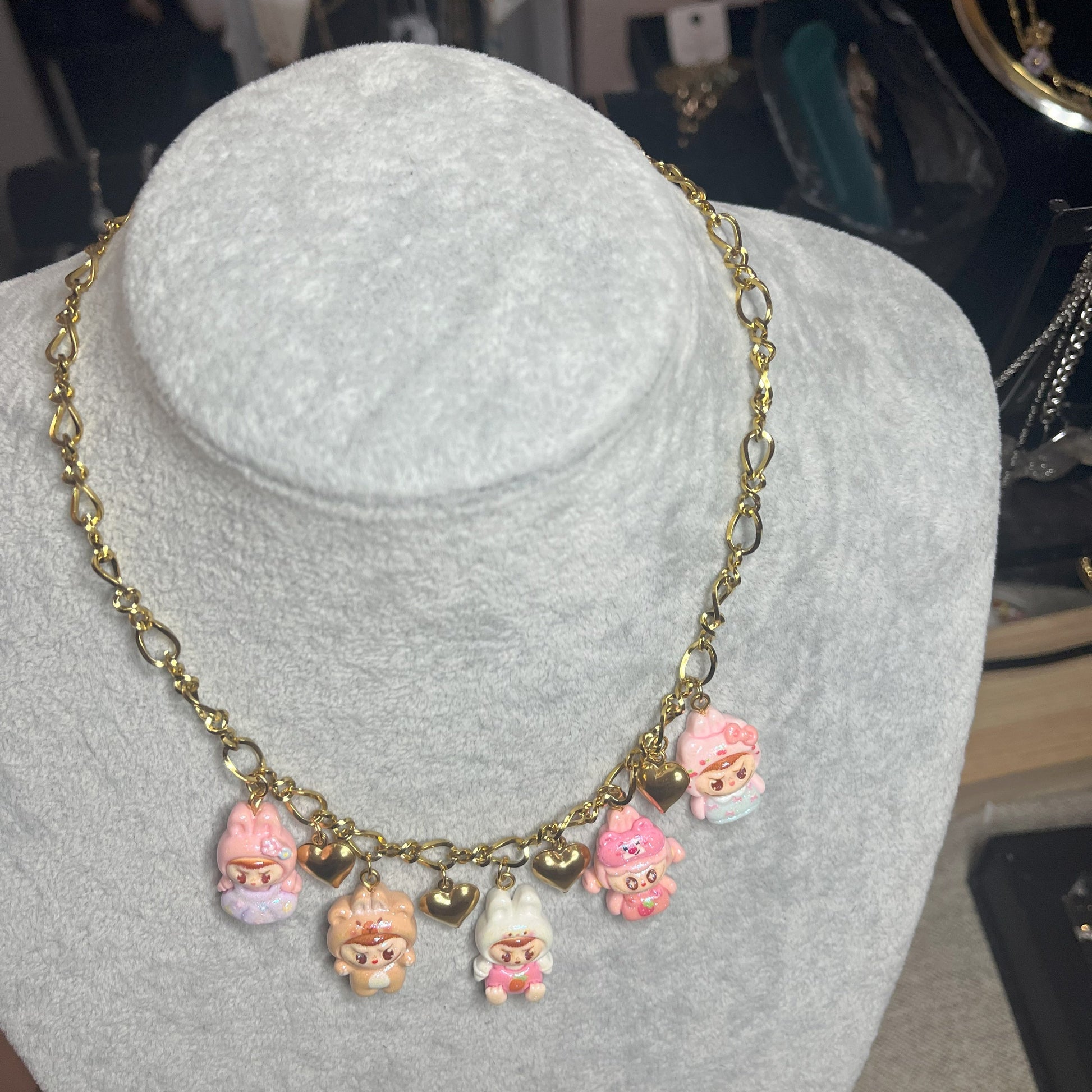 Collana con catena dorata e charms kawaii colorati a forma di personaggi cute, esposta su busto bianco