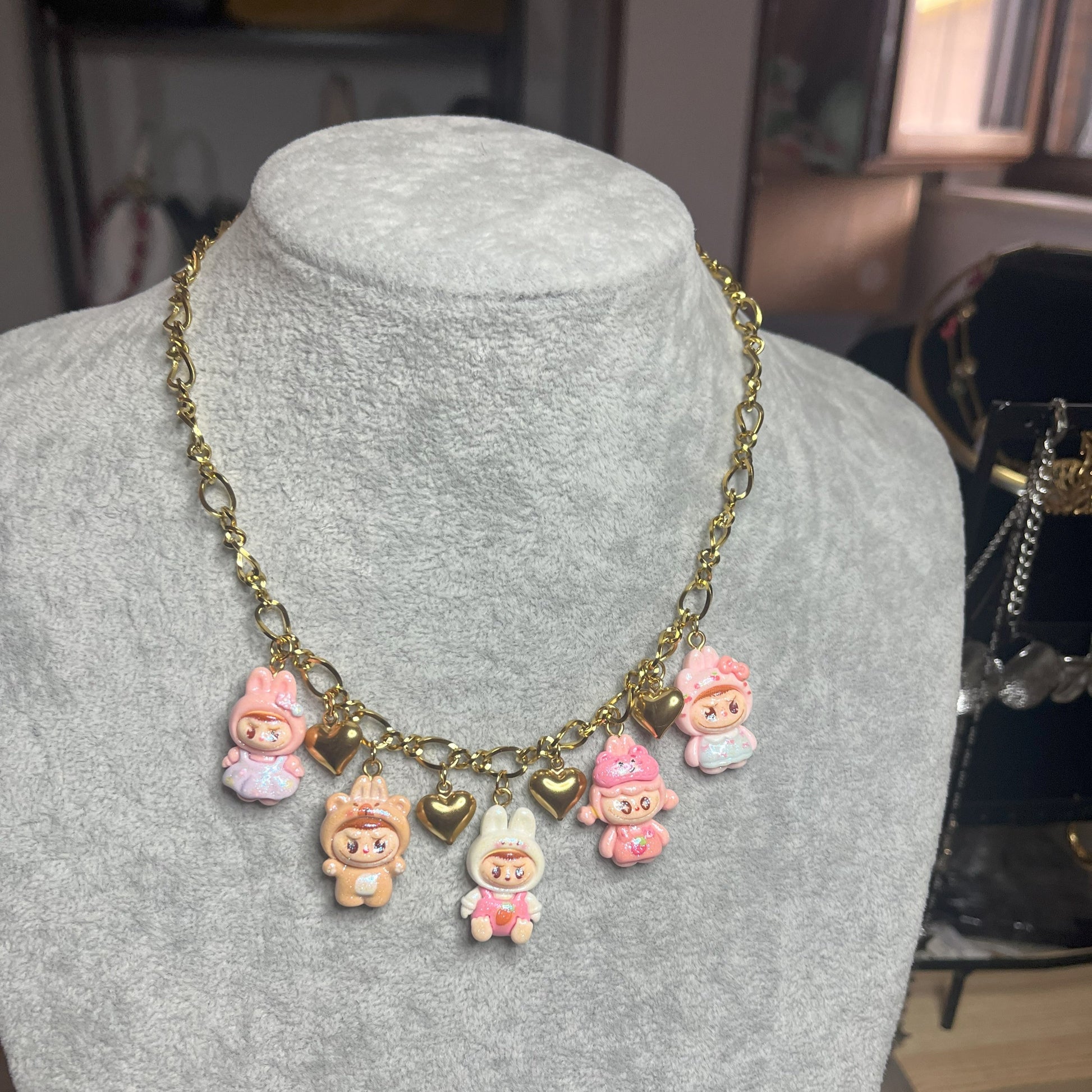 Collana con catena dorata e charms kawaii colorati a forma di personaggi cute, esposta su busto bianco