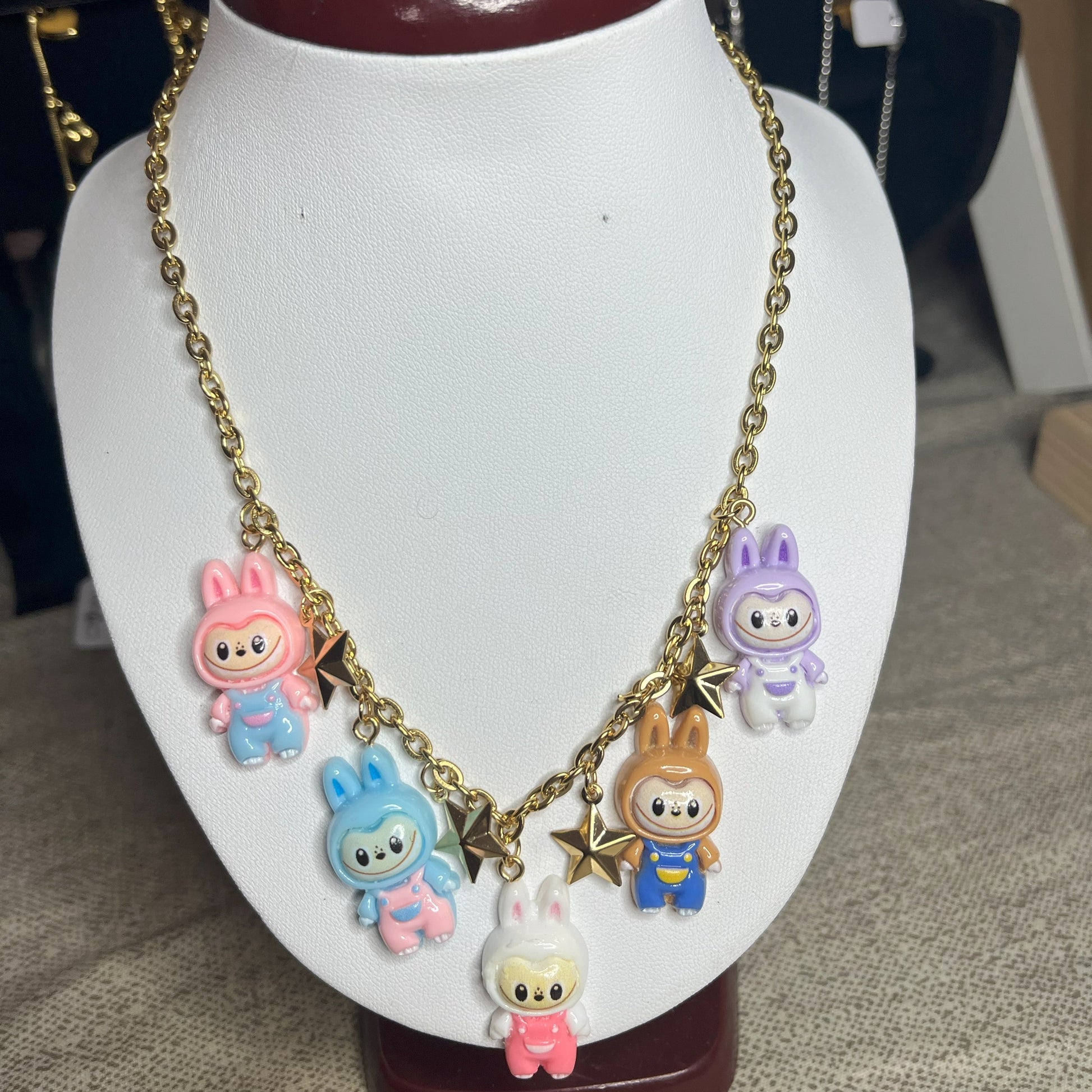 Collana con catena dorata e charms kawaii colorati a forma di personaggi cute, esposta su busto bianco