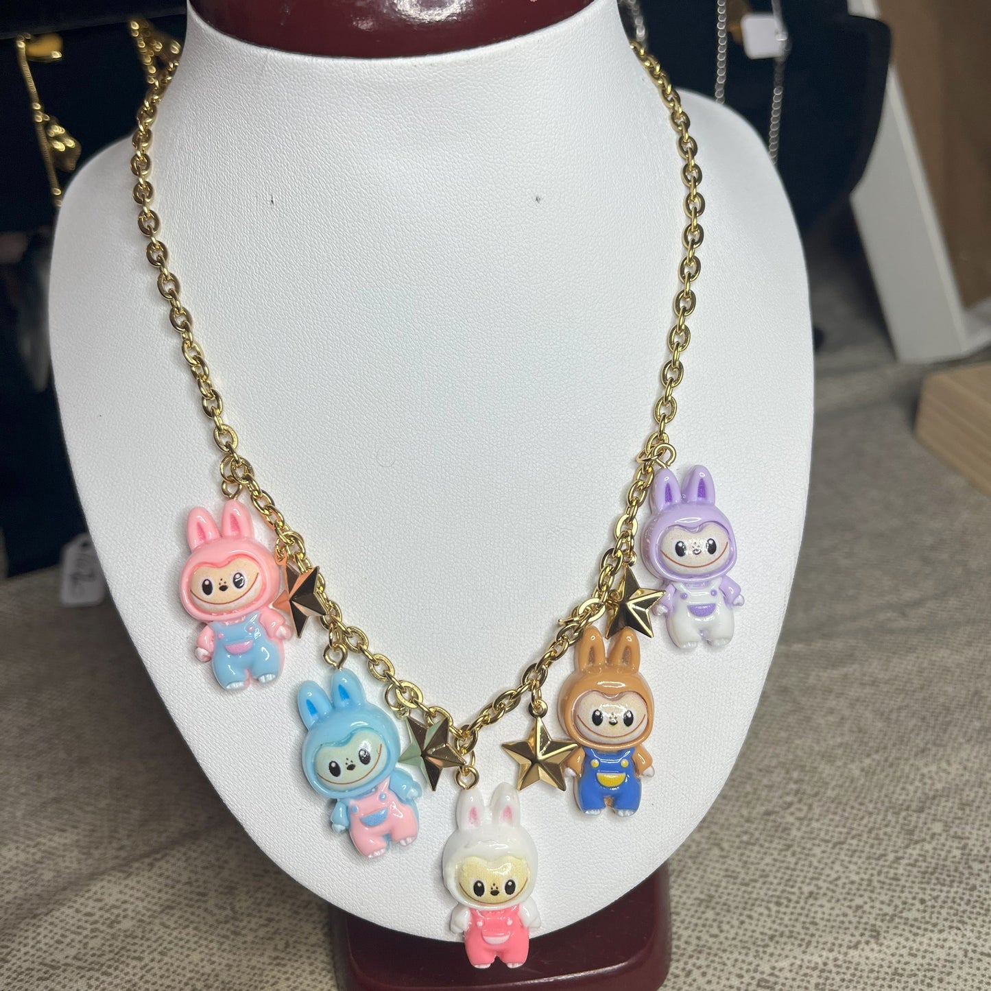 Collana con catena dorata e charms kawaii colorati a forma di personaggi cute, esposta su busto bianco