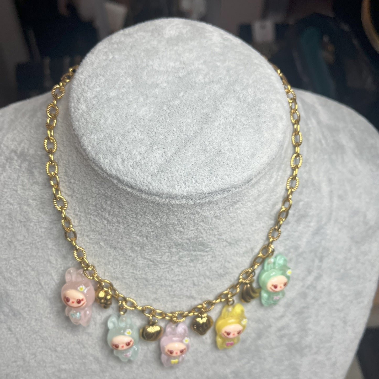 Collana con catena dorata e charms kawaii colorati a forma di personaggi cute, esposta su busto bianco