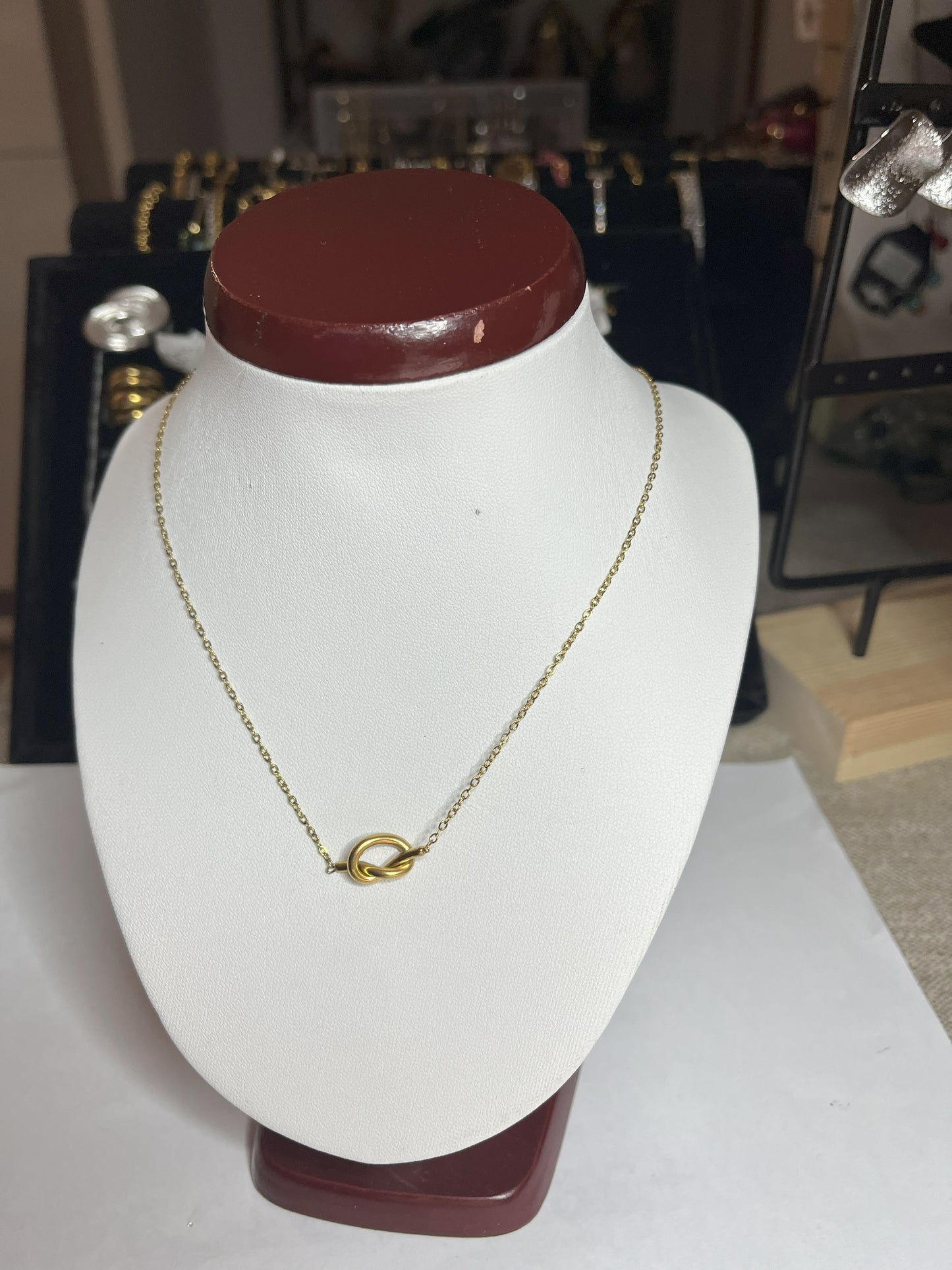 Collana Love Knot con pendente a nodo intrecciato dorato su catena delicata, simbolo di amore eterno esposto su busto bianco