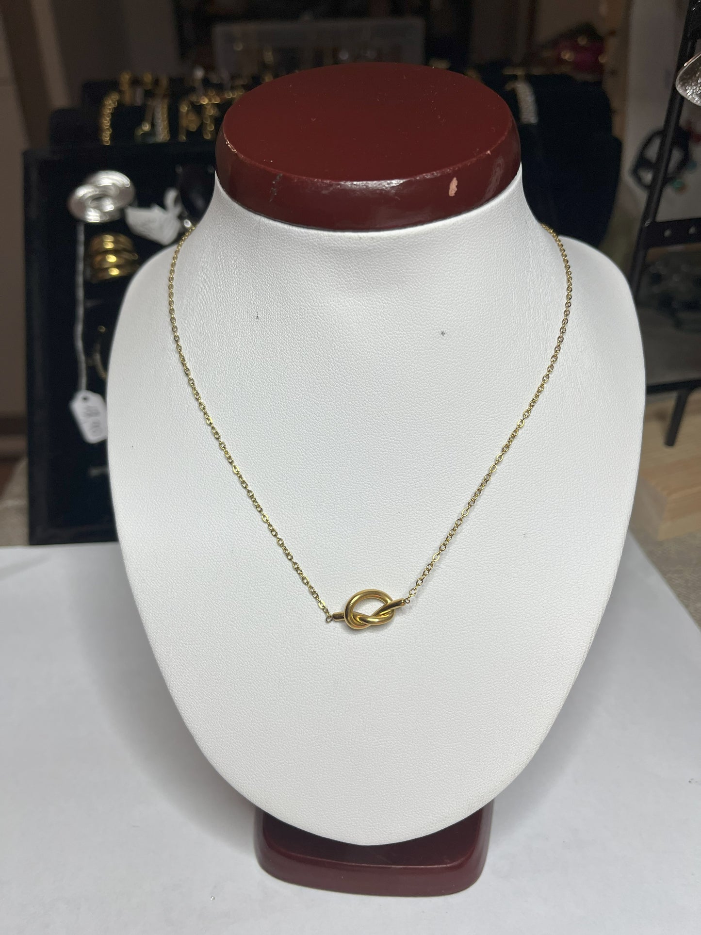Collana Love Knot con pendente a nodo intrecciato dorato su catena delicata, simbolo di amore eterno esposto su busto bianco