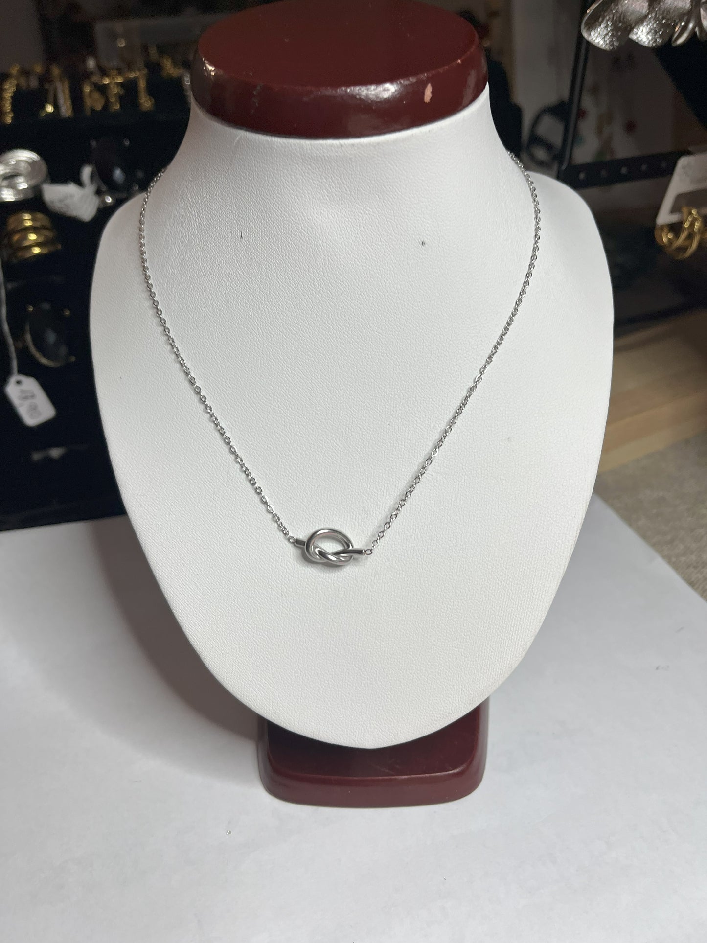 Collana Love Knot con pendente a nodo intrecciato dorato su catena delicata, simbolo di amore eterno esposto su busto bianco