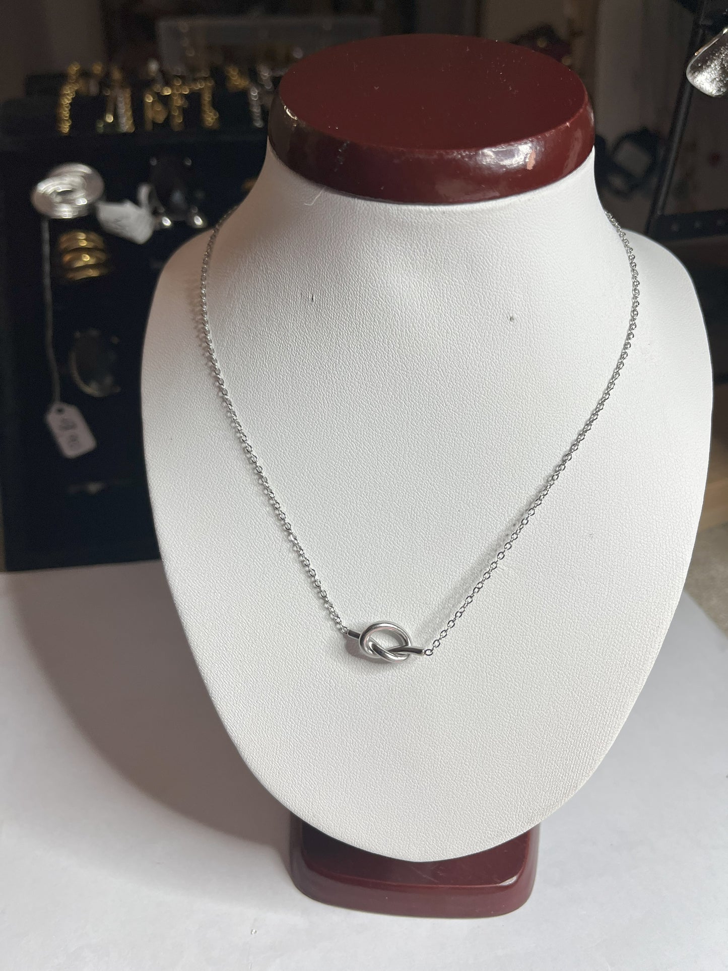 Collana Love Knot con pendente a nodo intrecciato dorato su catena delicata, simbolo di amore eterno esposto su busto bianco
