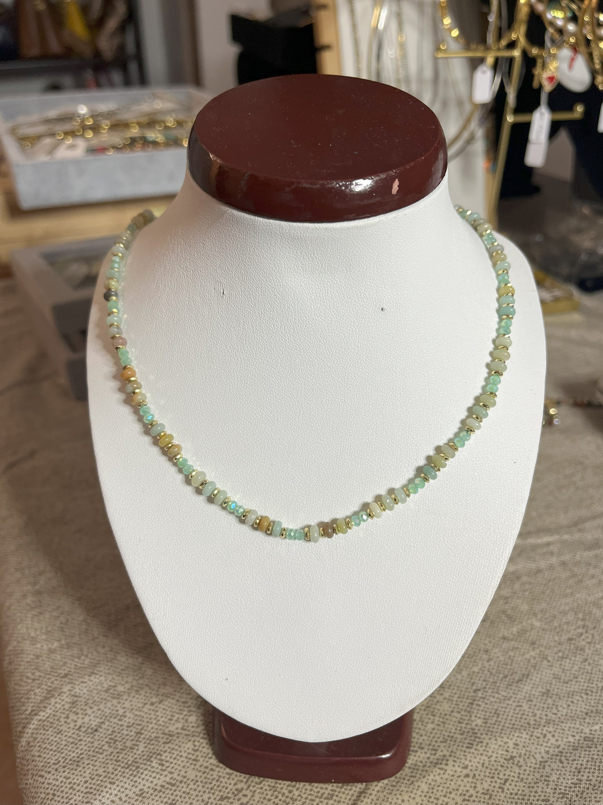 Collana Mosaico Prezioso disponibile in due varianti: multicolore con pietre rosse, verdi, blu e oro, e verde-oro con tonalità smeraldo e dorate, su espositore bianco