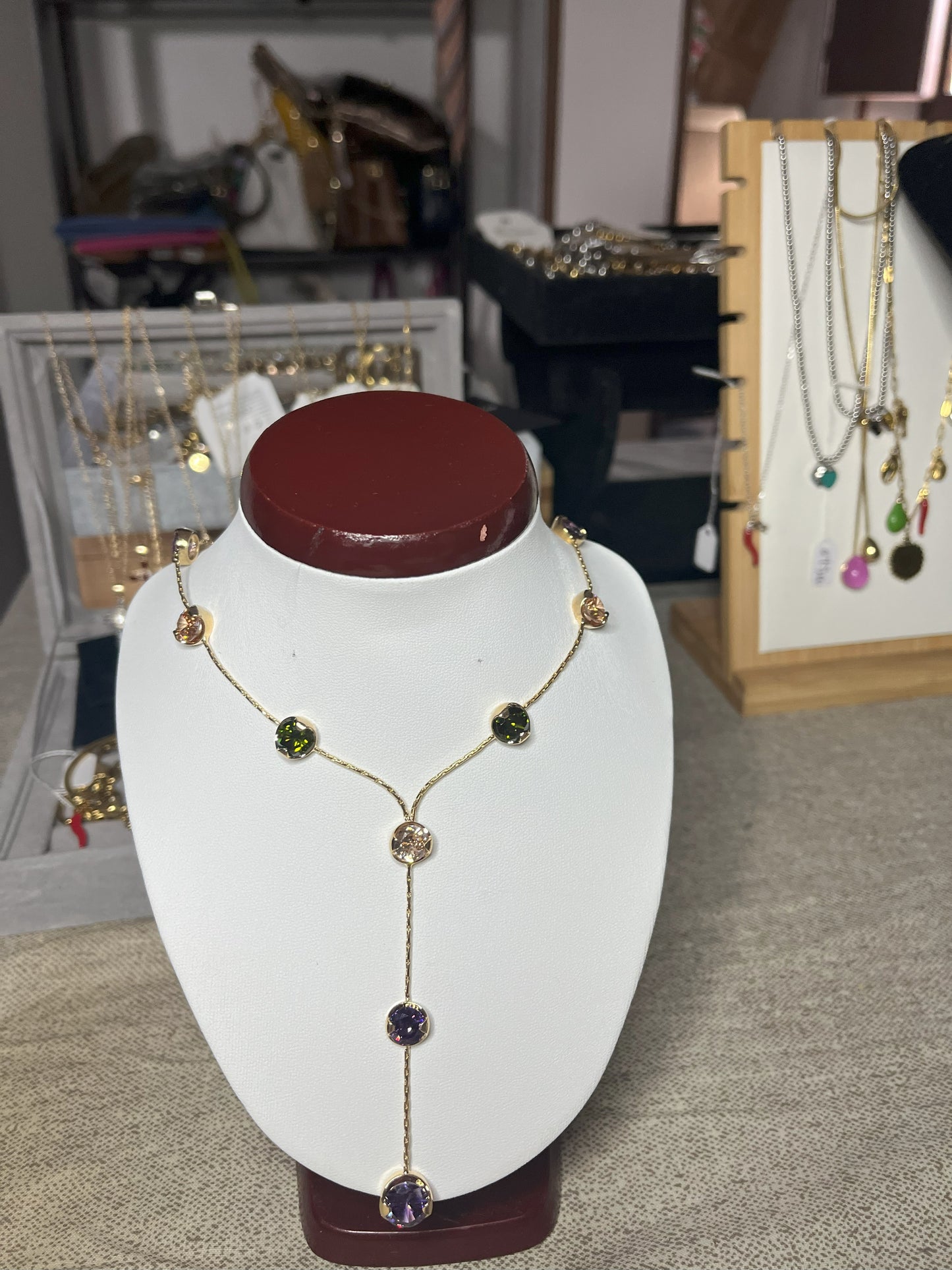 Collana Ottone e Cristalli Bohémien esposta su busto bianco, design asimmetrico con pendente lungo, cristalli verdi e viola incastonati in ottone dorato, stile bohémien elegante