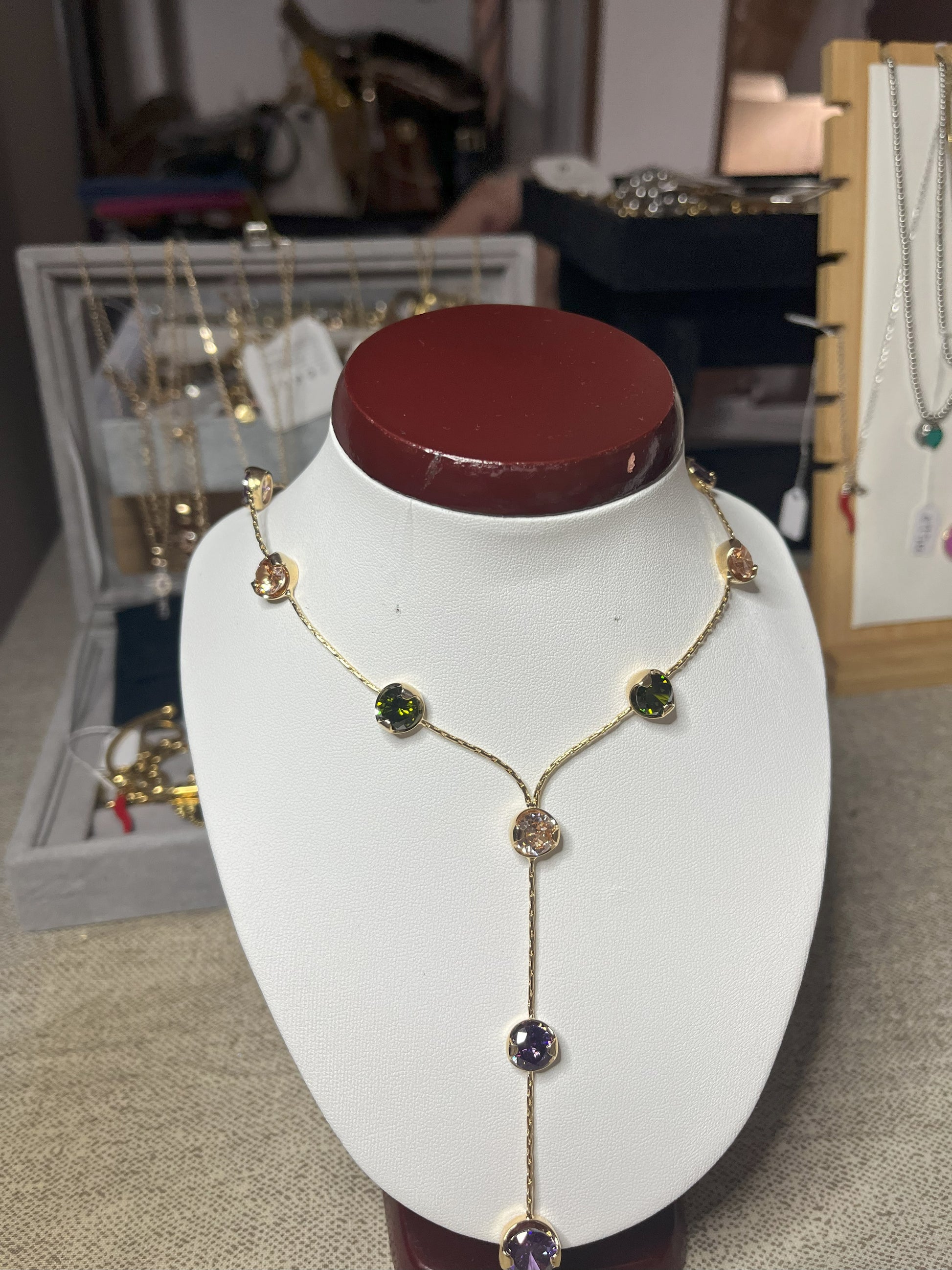 Collana Ottone e Cristalli Bohémien esposta su busto bianco, design asimmetrico con pendente lungo, cristalli verdi e viola incastonati in ottone dorato, stile bohémien elegante