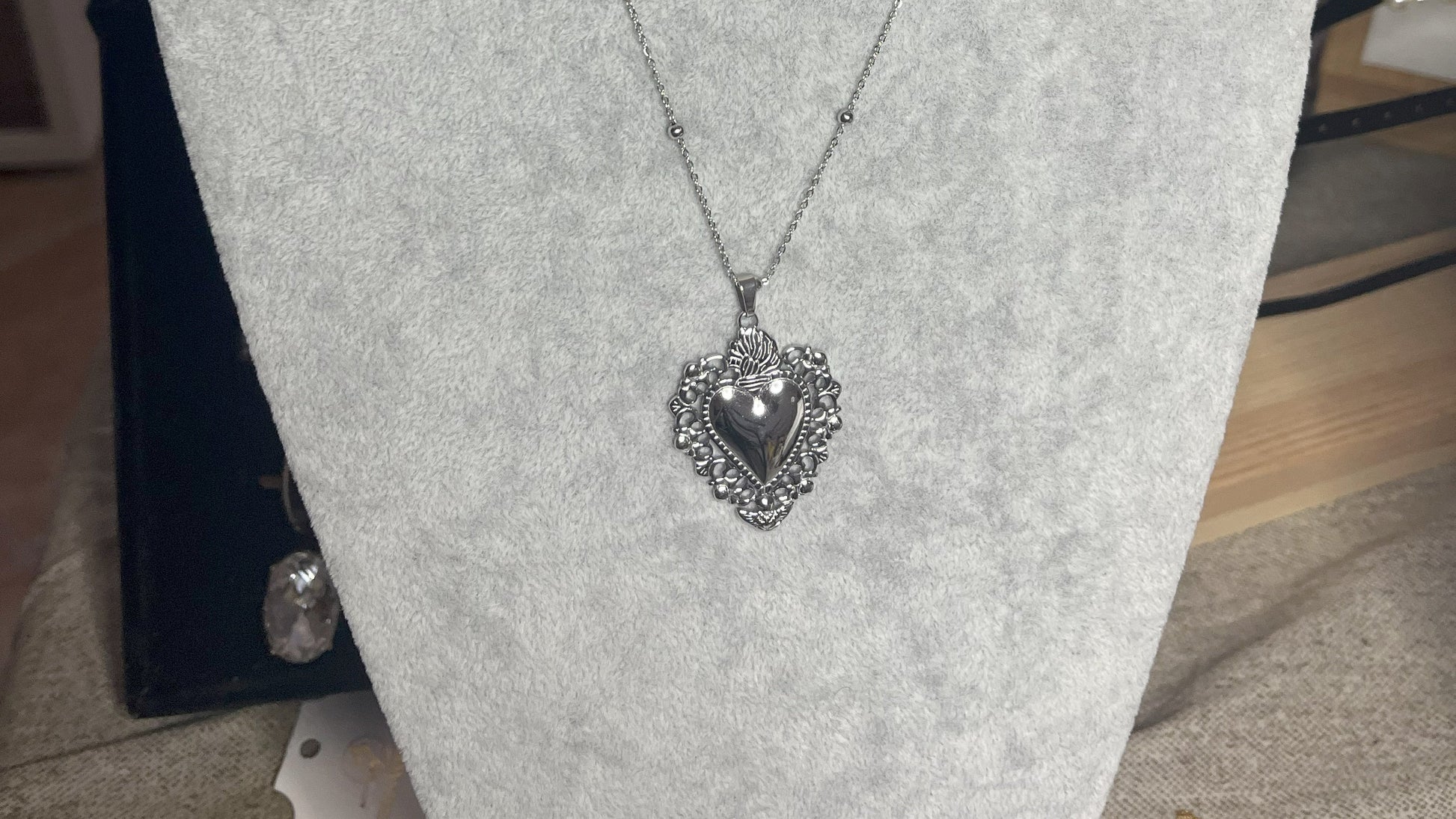 Collana Regina Cuori Sacri in acciaio premium placcato oro con ciondolo a cuore ornamentale barocco e catena decorativa con sfere, esposta su busto grigio