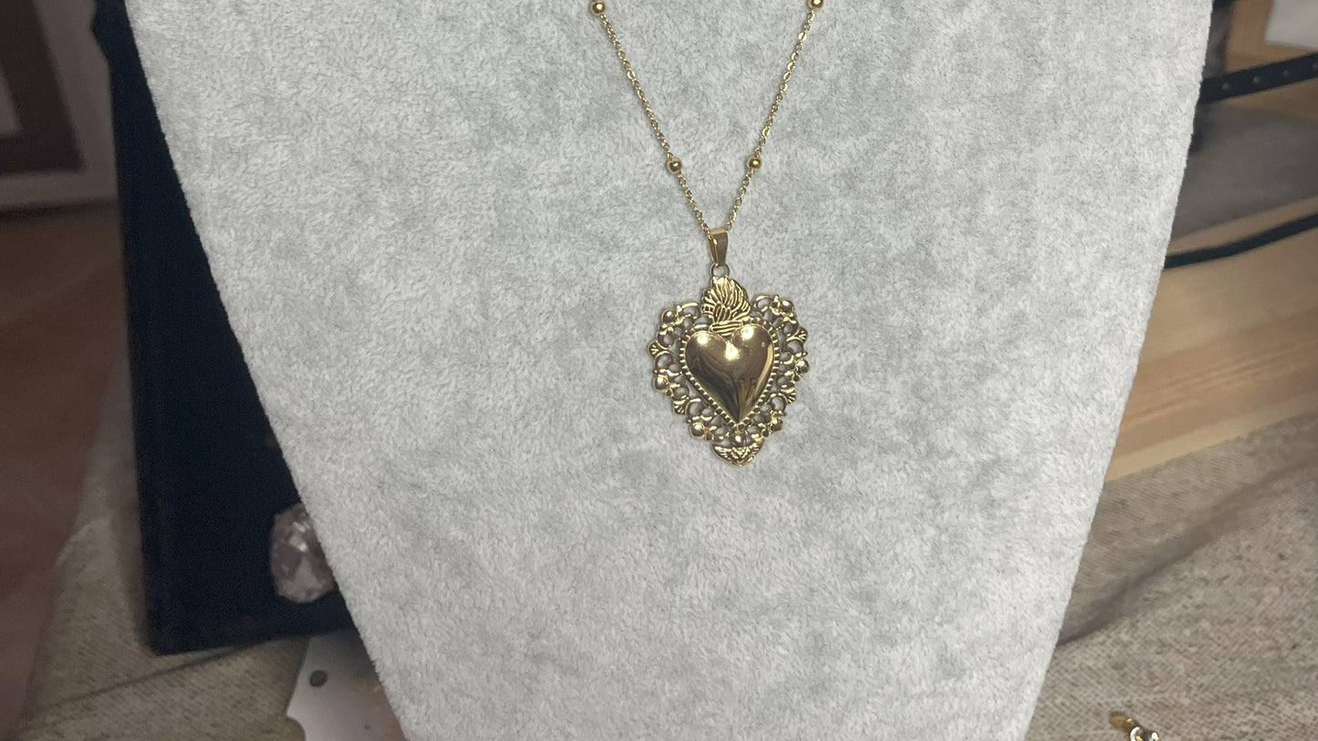 Collana Regina Cuori Sacri in acciaio premium placcato oro con ciondolo a cuore ornamentale barocco e catena decorativa con sfere, esposta su busto grigio