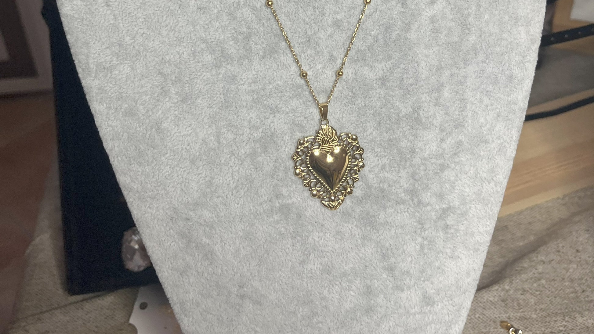 Collana Regina Cuori Sacri in acciaio premium placcato oro con ciondolo a cuore ornamentale barocco e catena decorativa con sfere, esposta su busto grigio