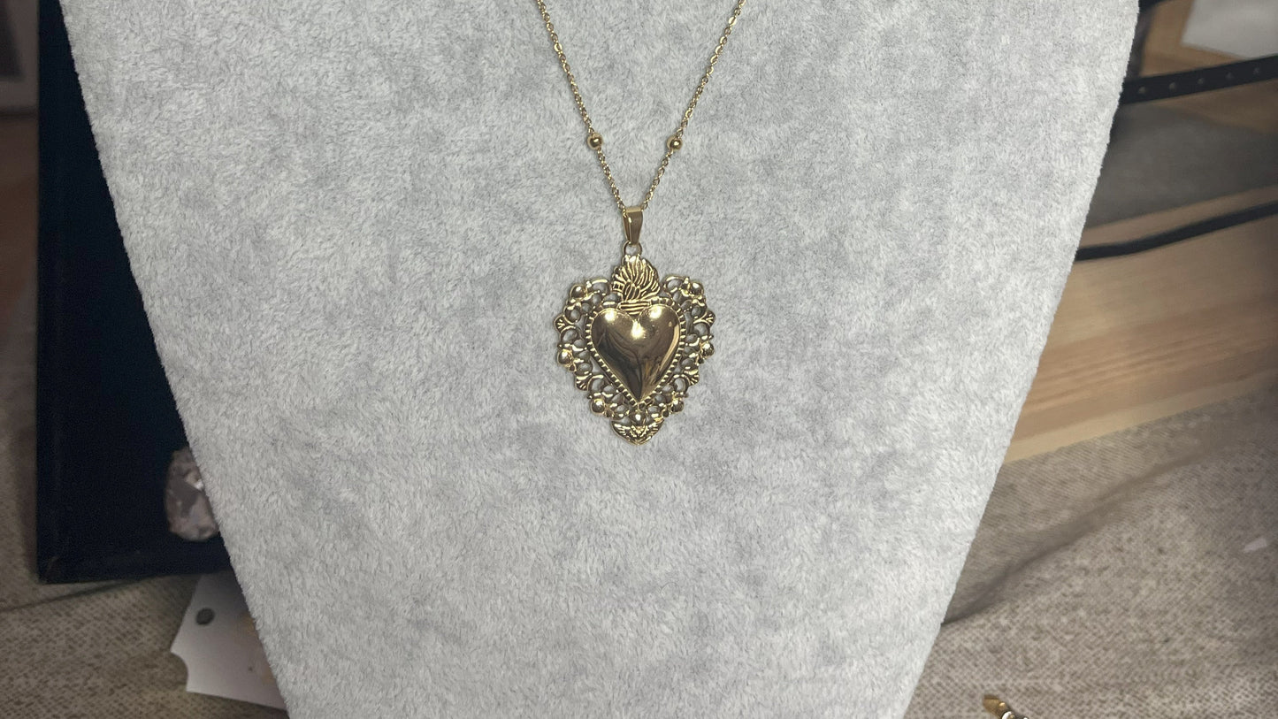 Collana Regina Cuori Sacri in acciaio premium placcato oro con ciondolo a cuore ornamentale barocco e catena decorativa con sfere, esposta su busto grigio