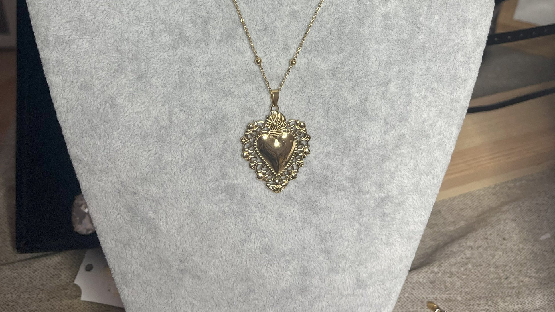 Collana Regina Cuori Sacri in acciaio premium placcato oro con ciondolo a cuore ornamentale barocco e catena decorativa con sfere, esposta su busto grigio