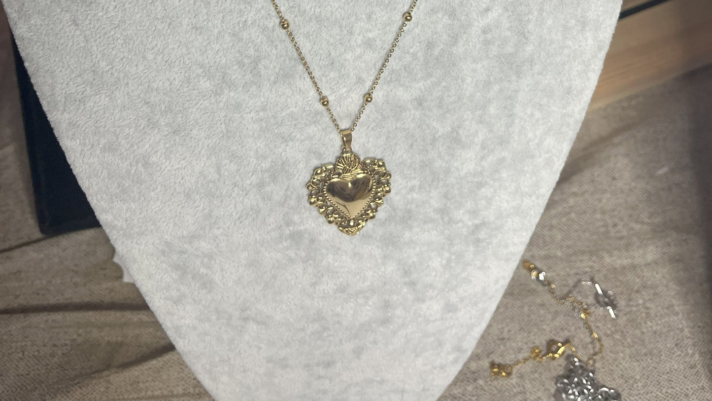 Collana Regina Cuori Sacri in acciaio premium placcato oro con ciondolo a cuore ornamentale barocco e catena decorativa con sfere, esposta su busto grigio