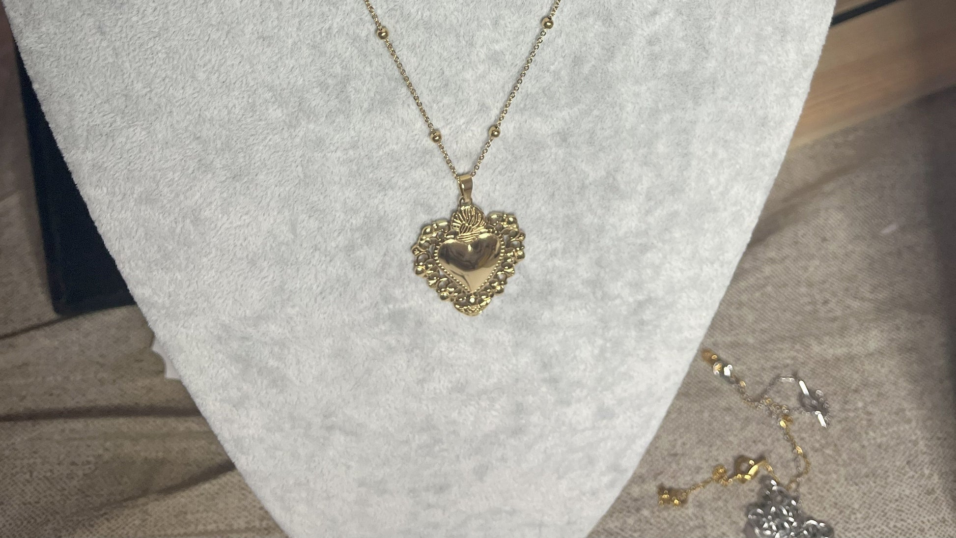 Collana Regina Cuori Sacri in acciaio premium placcato oro con ciondolo a cuore ornamentale barocco e catena decorativa con sfere, esposta su busto grigio