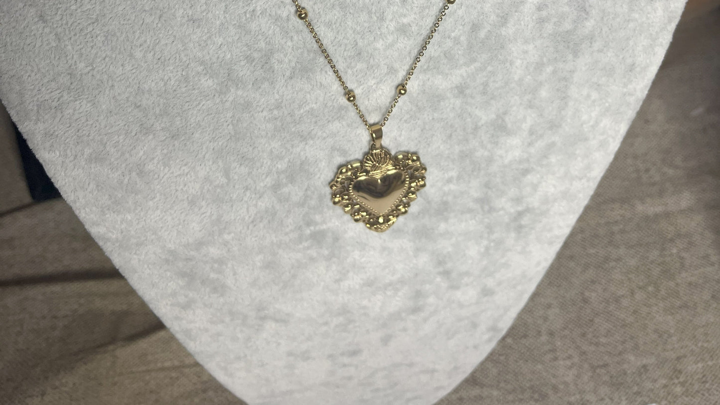Collana Regina Cuori Sacri in acciaio premium placcato oro con ciondolo a cuore ornamentale barocco e catena decorativa con sfere, esposta su busto grigio