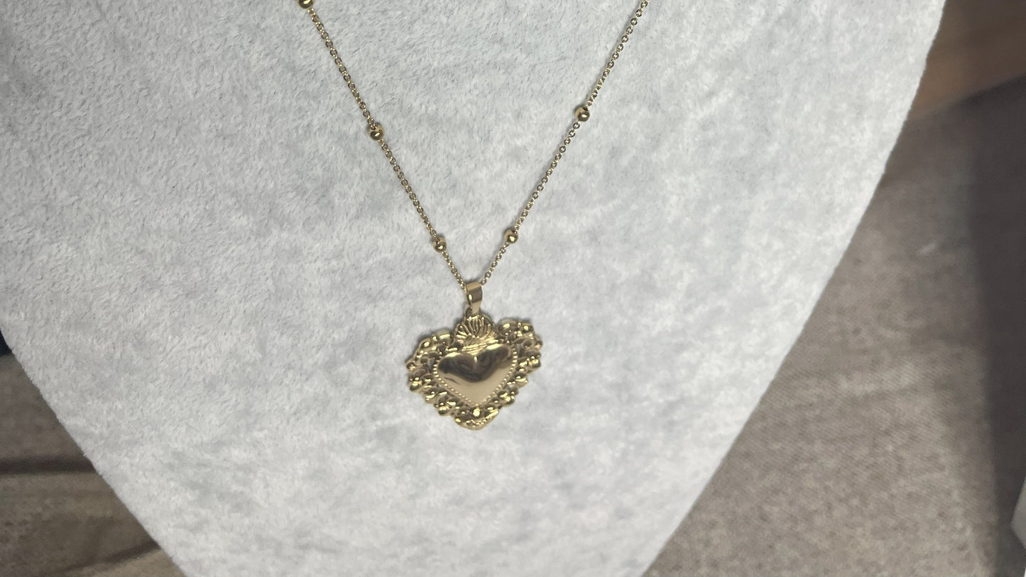 Collana Regina Cuori Sacri in acciaio premium placcato oro con ciondolo a cuore ornamentale barocco e catena decorativa con sfere, esposta su busto grigio