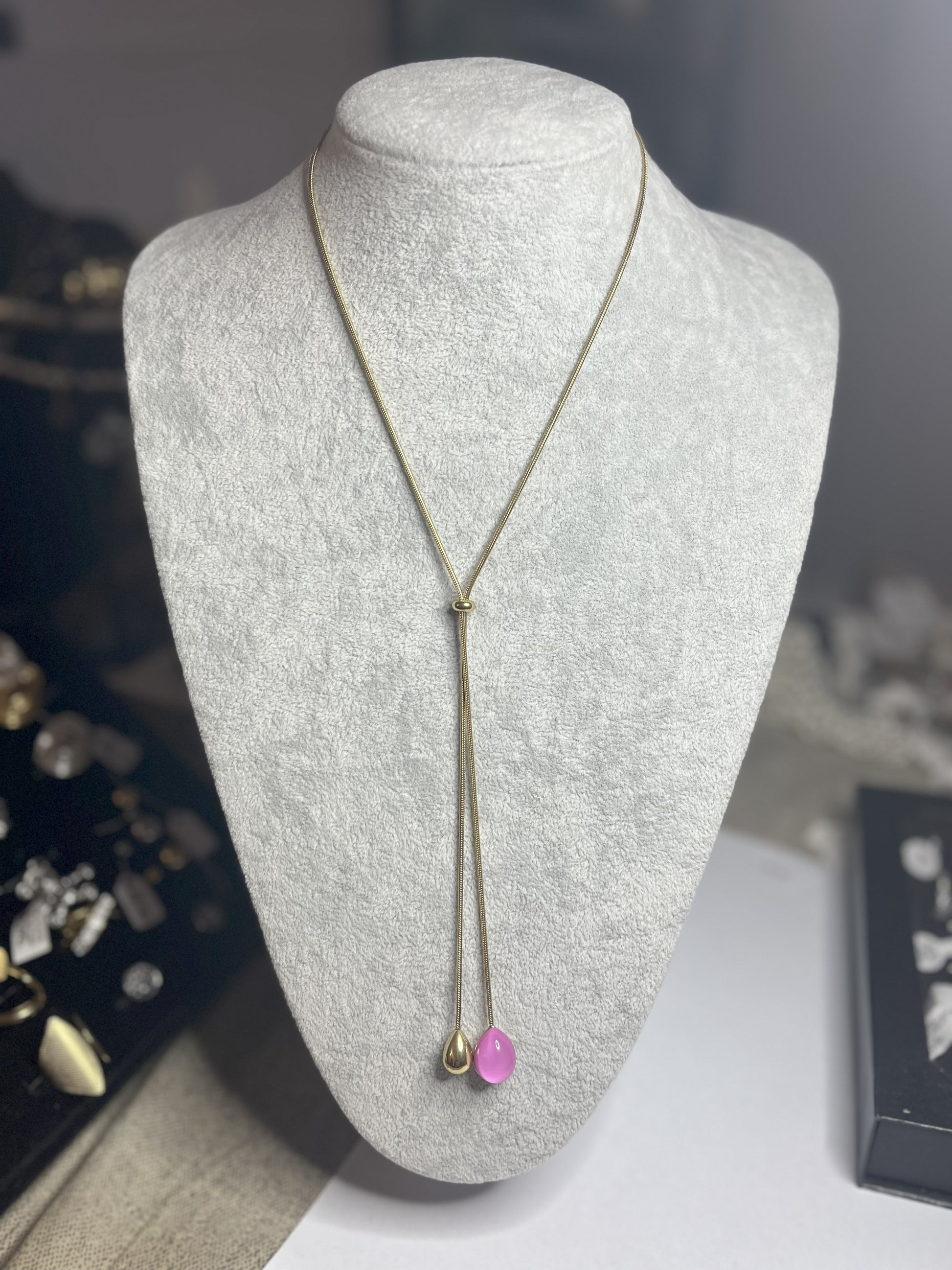 Collana Saliscendi Punto Fucsia in acciaio premium placcato oro con catena regolabile e terminale fucsia vibrante, esposta su busto grigio