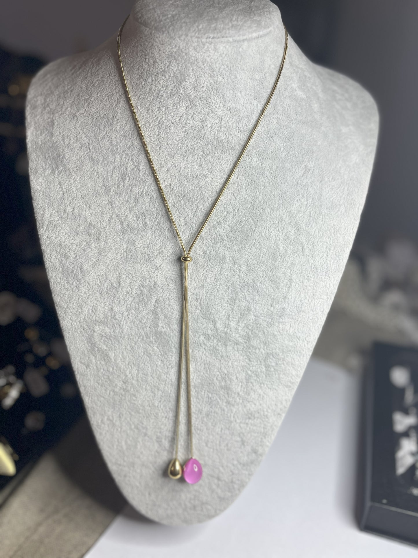 Collana Saliscendi Punto Fucsia in acciaio premium placcato oro con catena regolabile e terminale fucsia vibrante, esposta su busto grigio