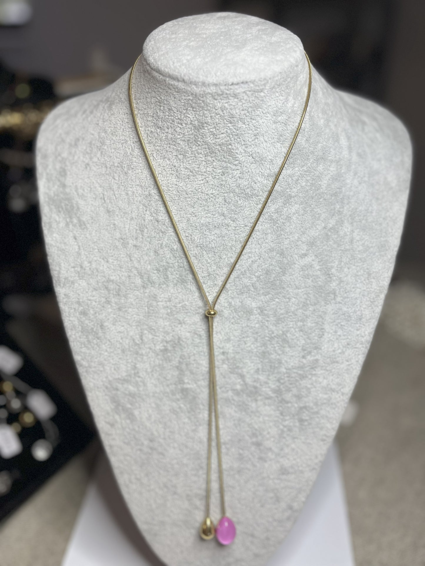 Collana Saliscendi Punto Fucsia in acciaio premium placcato oro con catena regolabile e terminale fucsia vibrante, esposta su busto grigio
