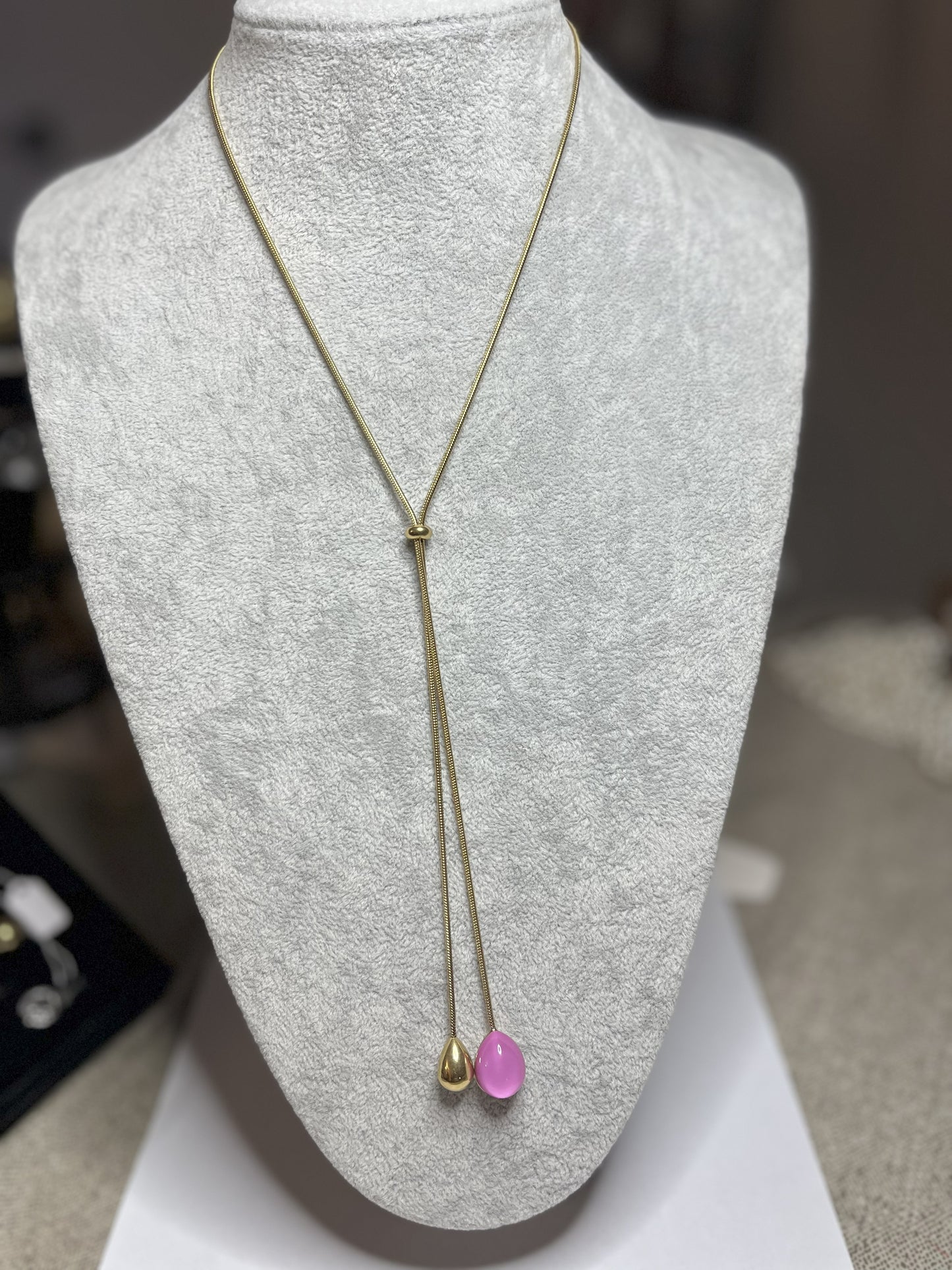Collana Saliscendi Punto Fucsia in acciaio premium placcato oro con catena regolabile e terminale fucsia vibrante, esposta su busto grigio