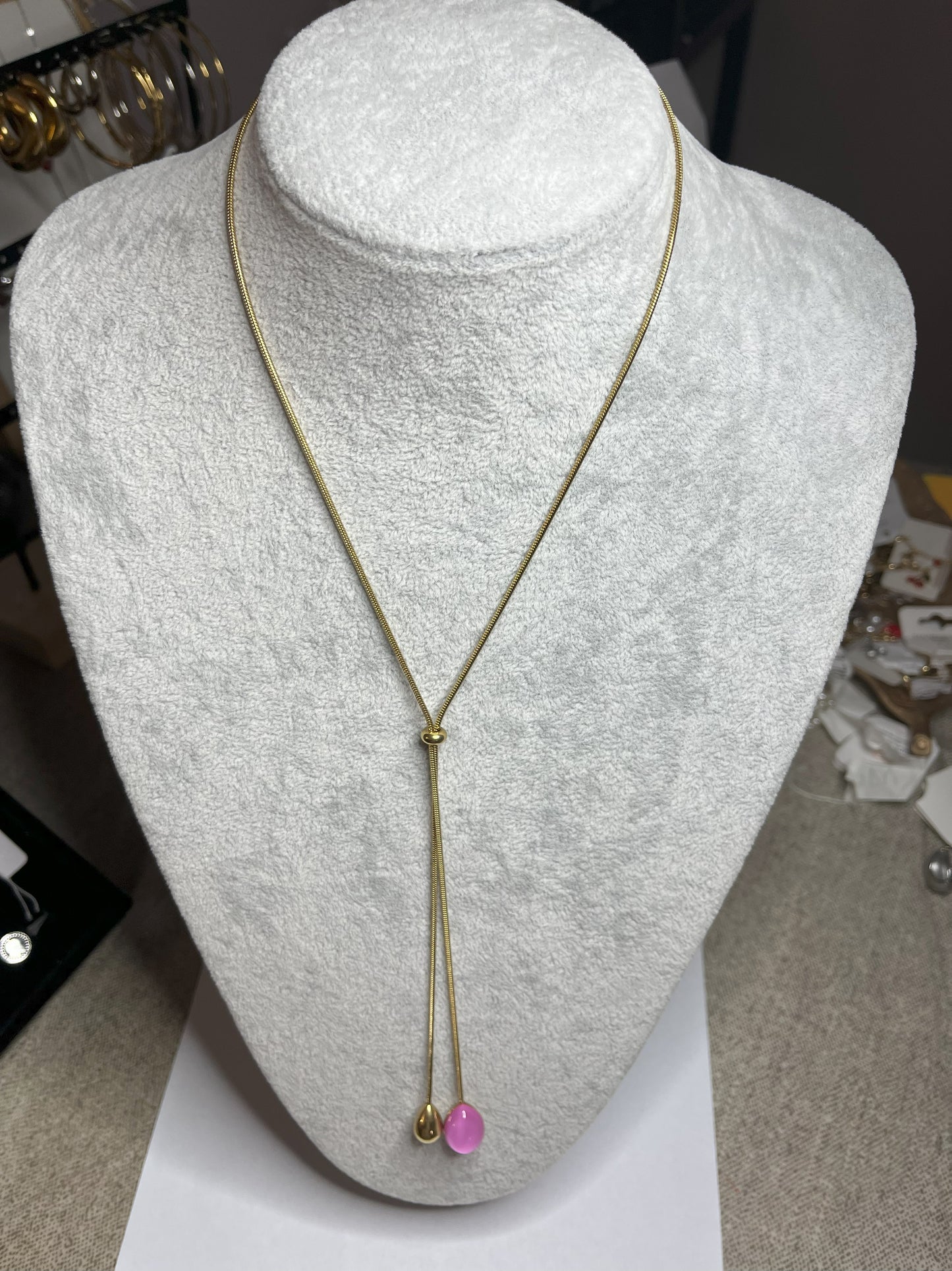 Collana Saliscendi Punto Fucsia in acciaio premium placcato oro con catena regolabile e terminale fucsia vibrante, esposta su busto grigio