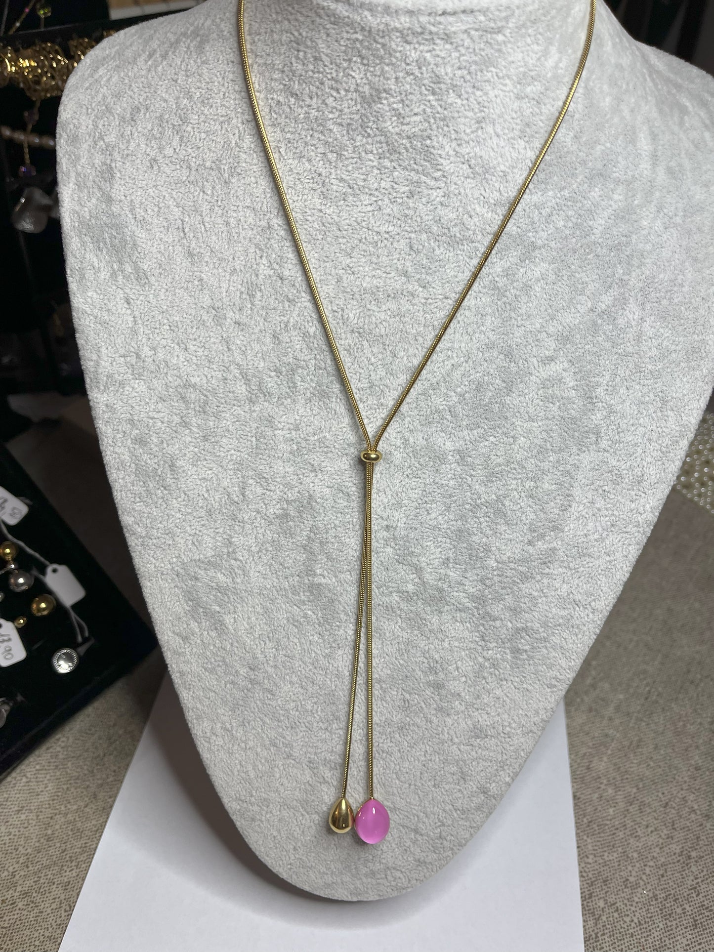 Collana Saliscendi Punto Fucsia in acciaio premium placcato oro con catena regolabile e terminale fucsia vibrante, esposta su busto grigio