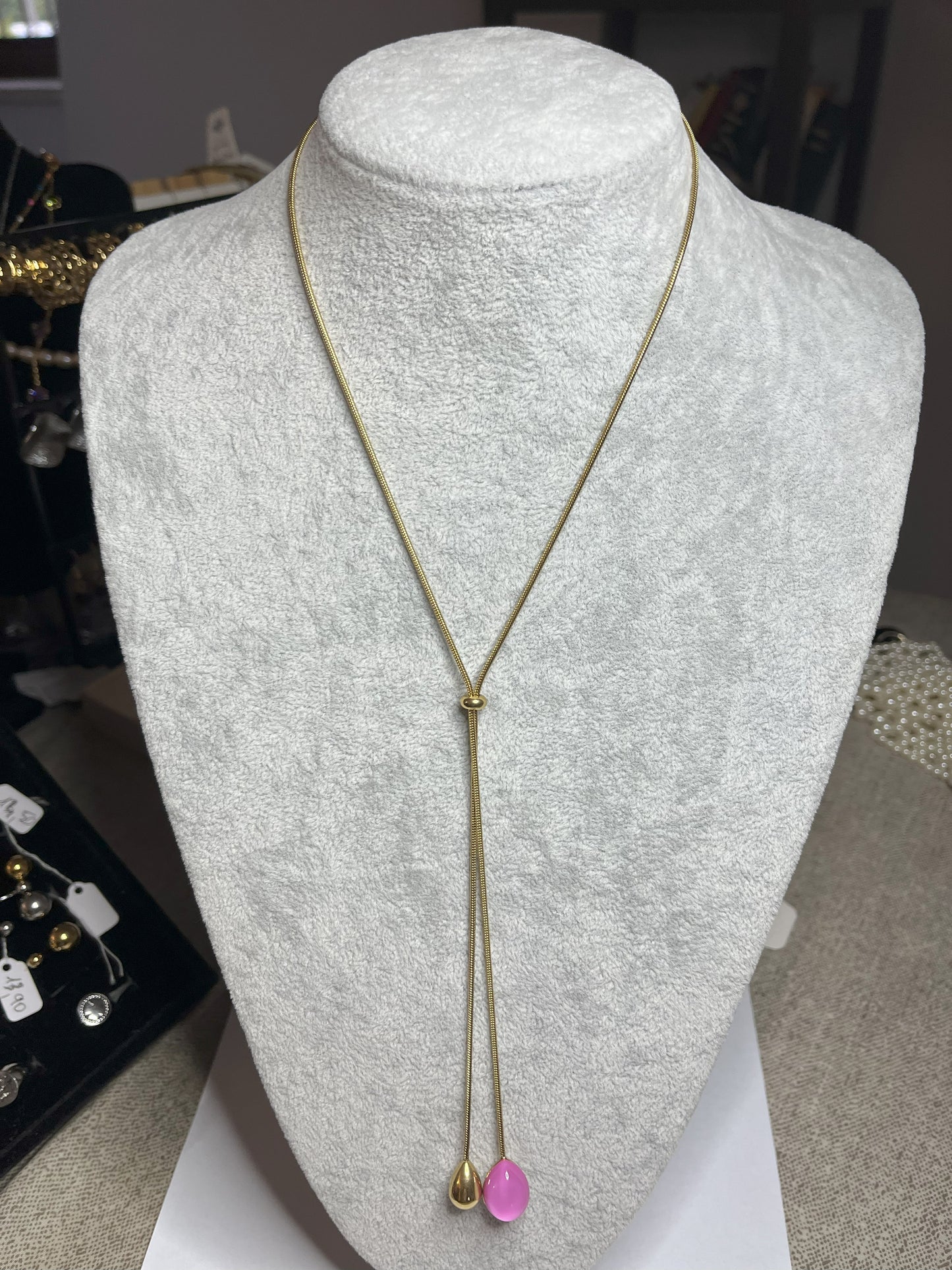 Collana Saliscendi Punto Fucsia in acciaio premium placcato oro con catena regolabile e terminale fucsia vibrante, esposta su busto grigio