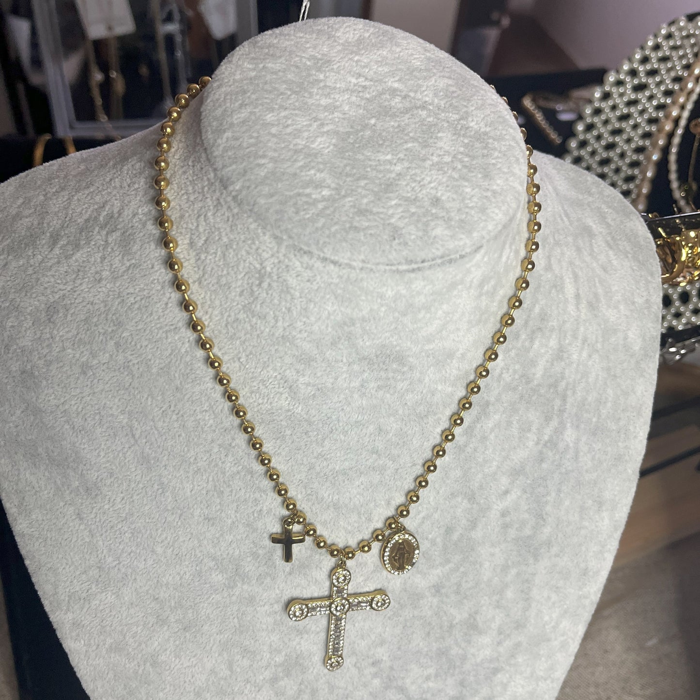 Collana Sfere Croce in acciaio premium placcato oro con catena a sfere e ciondolo croce decorato, esposta su busto grigio