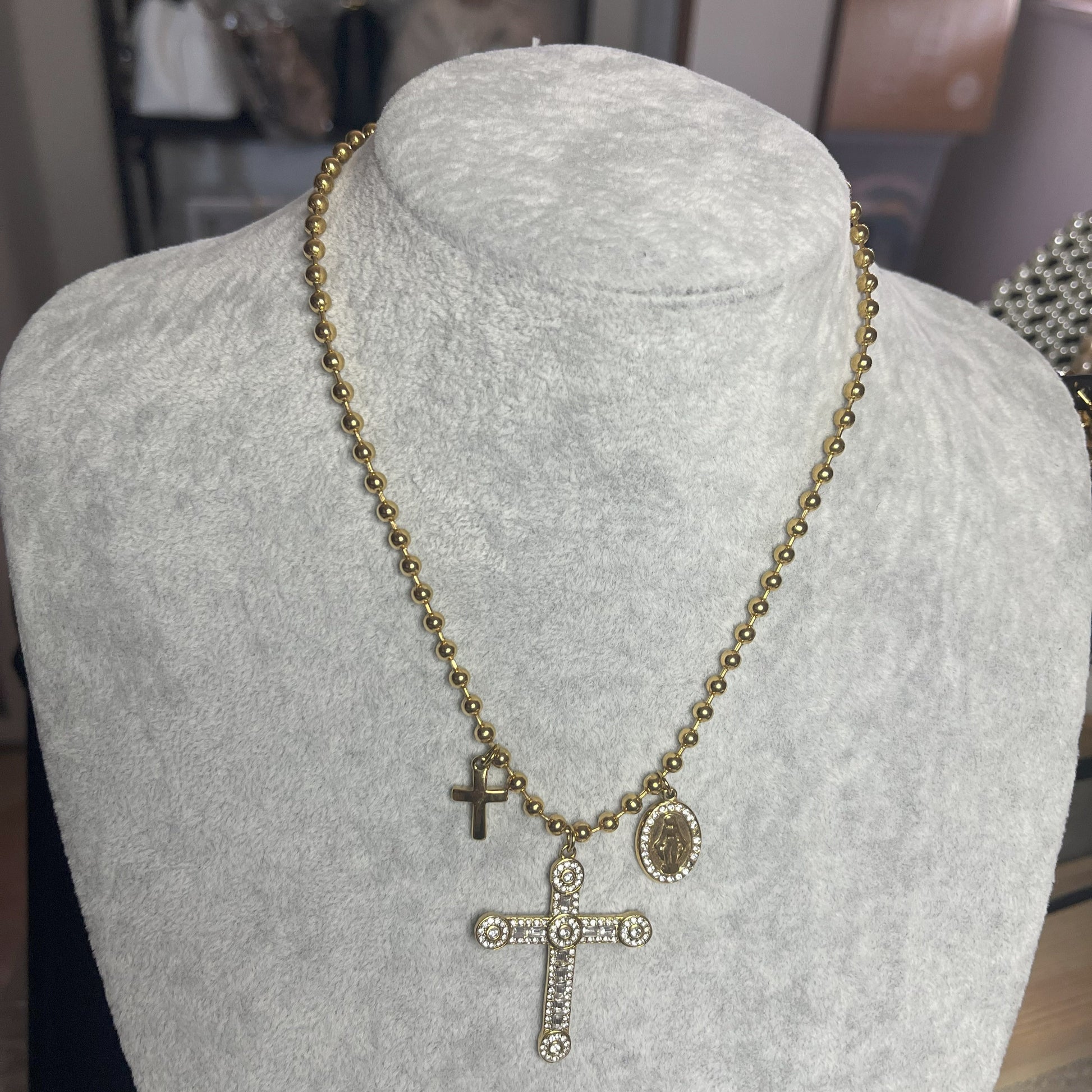 Collana Sfere Croce in acciaio premium placcato oro con catena a sfere e ciondolo croce decorato, esposta su busto grigio