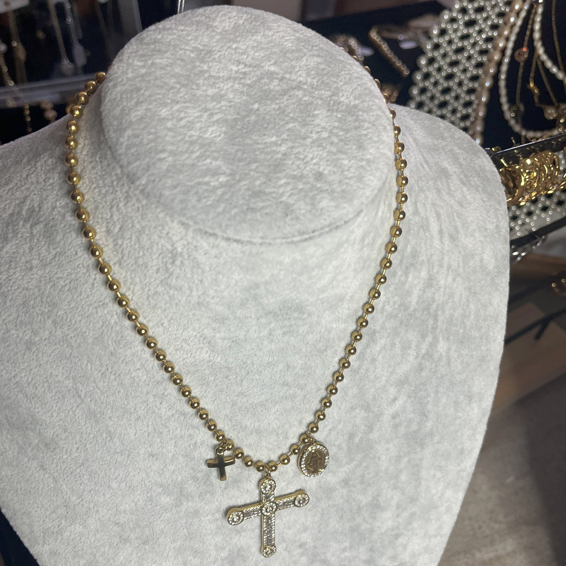 Collana Sfere Croce in acciaio premium placcato oro con catena a sfere e ciondolo croce decorato, esposta su busto grigio