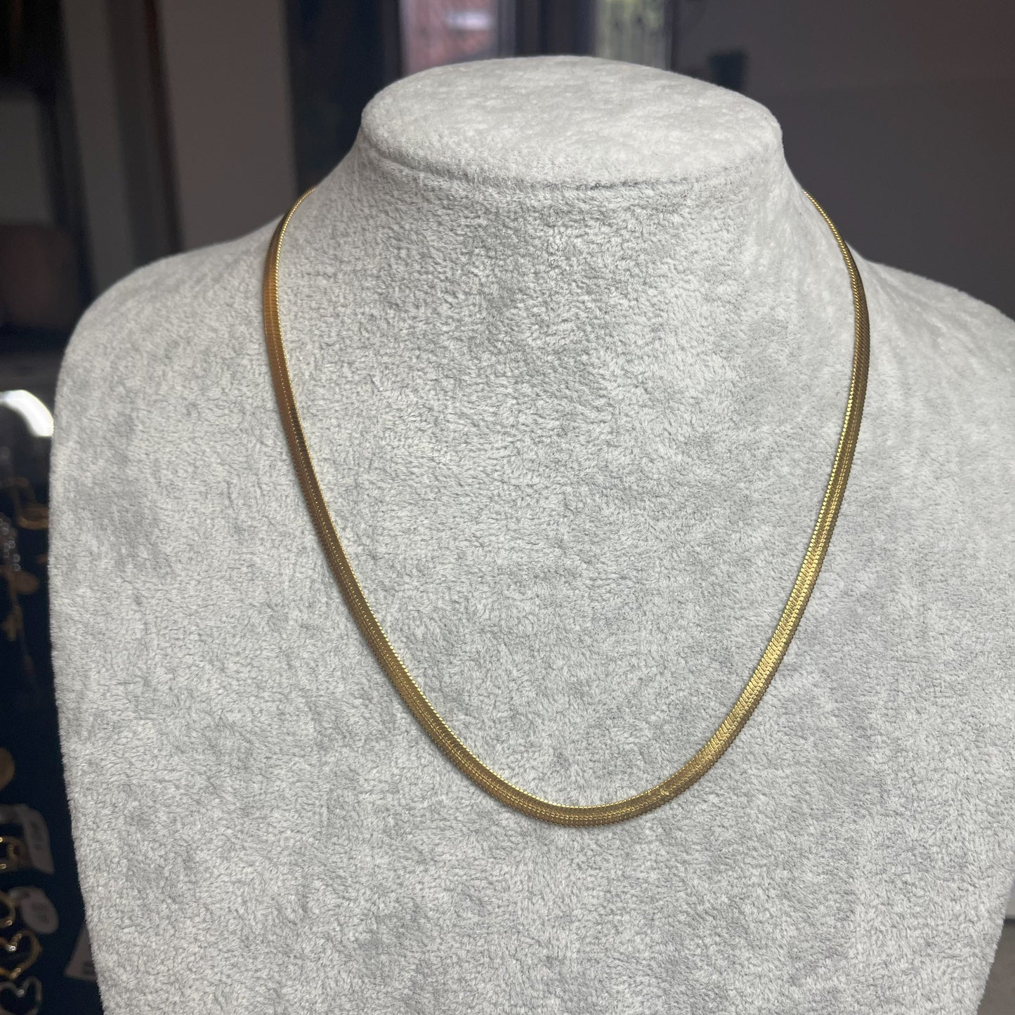 Collana Snake in acciaio premium in placcatura argento, con design ultra-sottile fluido, esposta su busto grigio chiaro